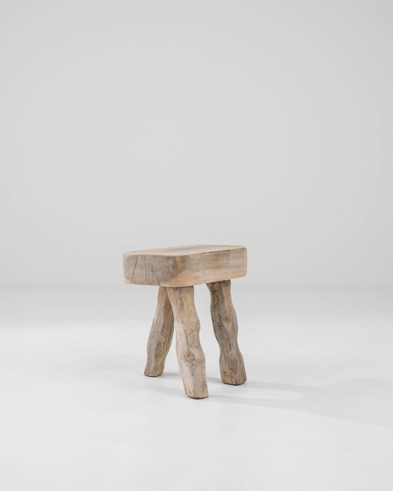A wooden stool created in 1900s France. Simple, rustic, and yet surprisingly elegant, this curious stool radiates with one of a kind charm. A tripod of gently carved legs offsets the stool just so, giving almost the appearance of a creature