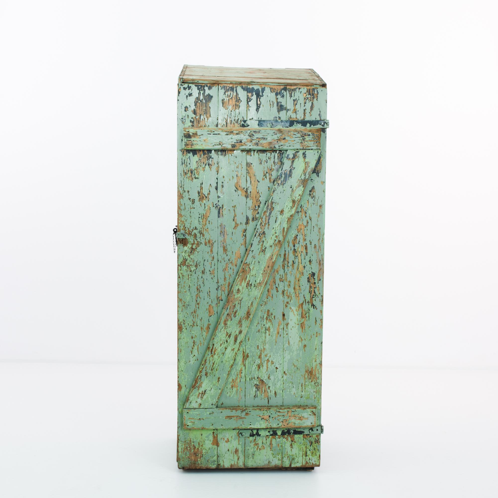 A single door wooden cabinet from Czechia circa 1950. This rustic storage locker clasps closed on sturdy steel hardware, prepared to be locked firmly shut. An elemental patina suggests outdoor use, flaking to reveal the golden hue of old growth