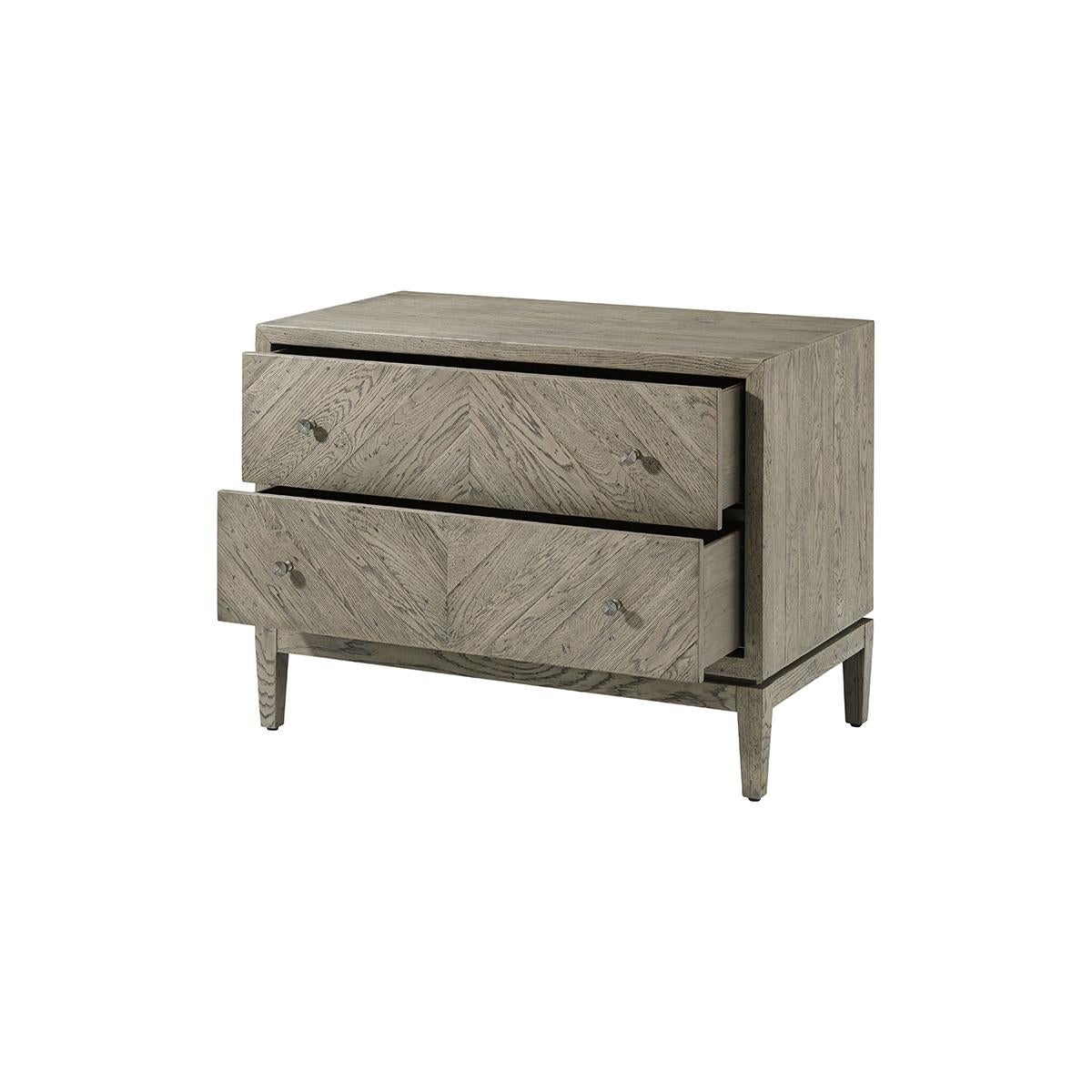 Rustic Greyed Oak two-drawer nightstand with a light oak rustic finish, herringbone diamond parquetry design, two long drawers with vintage textured metal handles and raised on square tapered legs.

Dimensions: 35