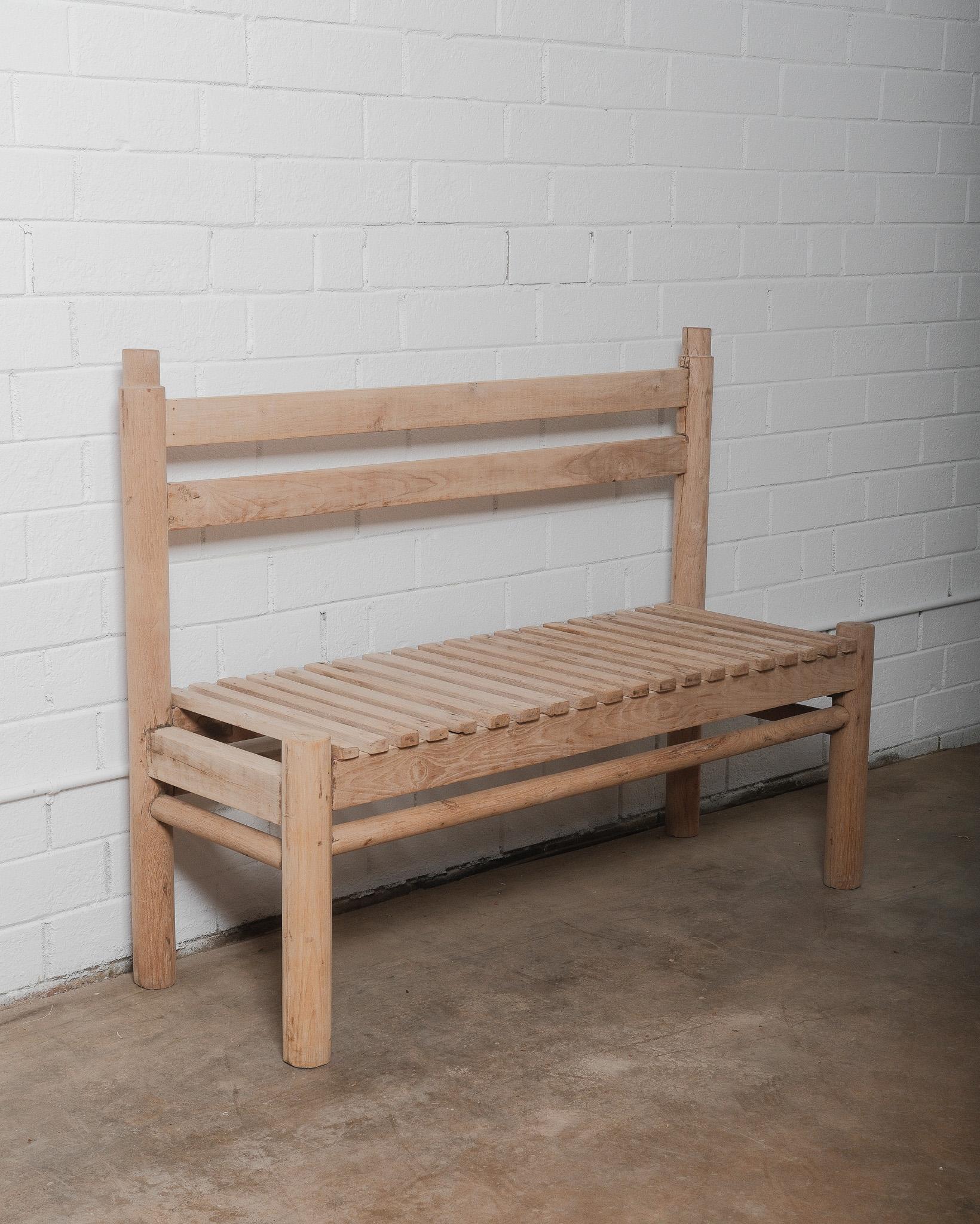 Ce banc rustique en bois fabriqué à la main est doté d'une belle assise simple à lattes et d'un dossier robuste, dégageant un charme organique et naturel. Le bois brut, non fini, met en évidence le grain unique, les nœuds et les imperfections,