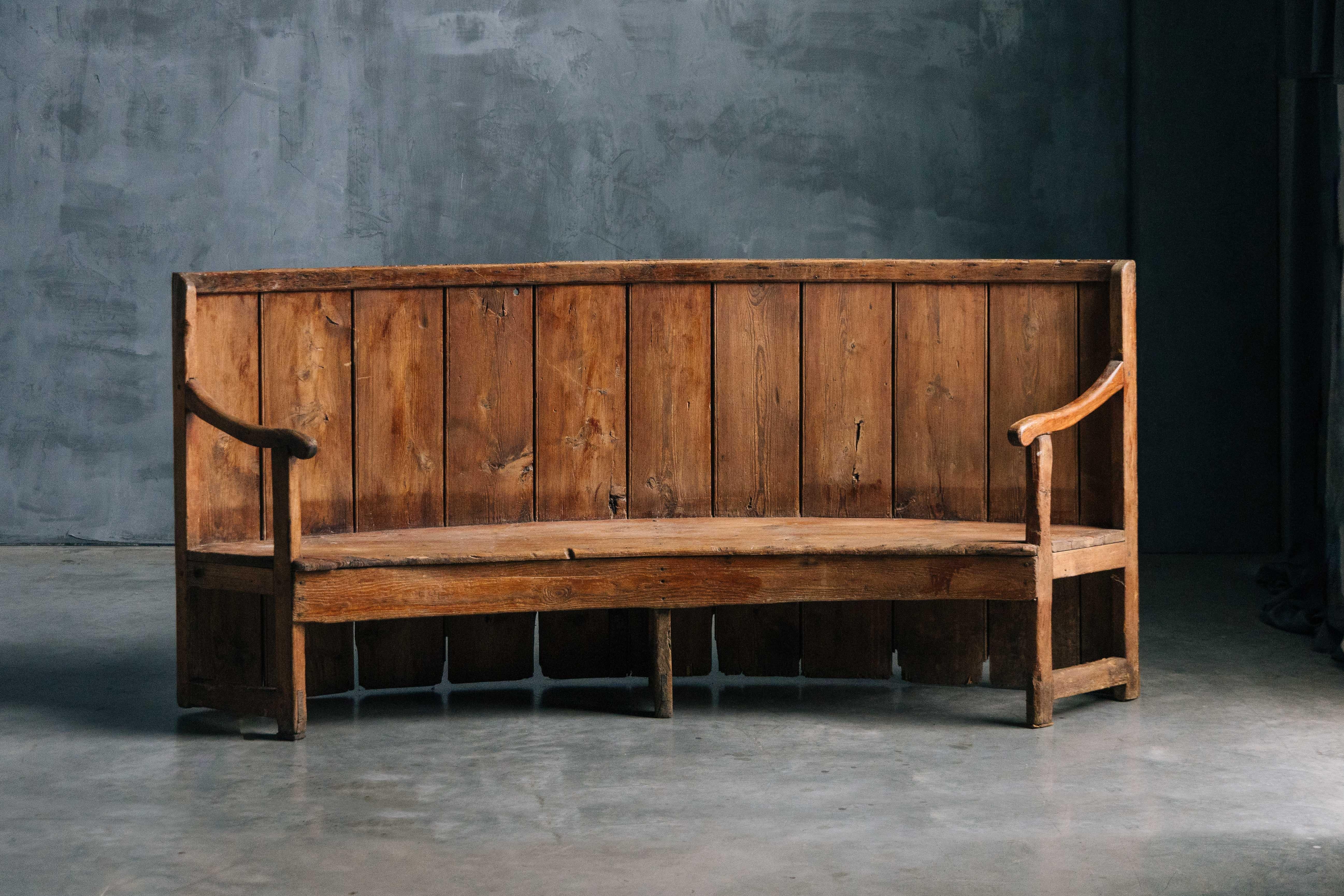 Antico sedile con schienale alto, risalente al XVIII secolo, che incarna il fascino rustico dei tradizionali mobili da taverna e locanda. Realizzato in legno massiccio, il suo design curvo e lo schienale alto sono ideali per sedersi intorno ai
