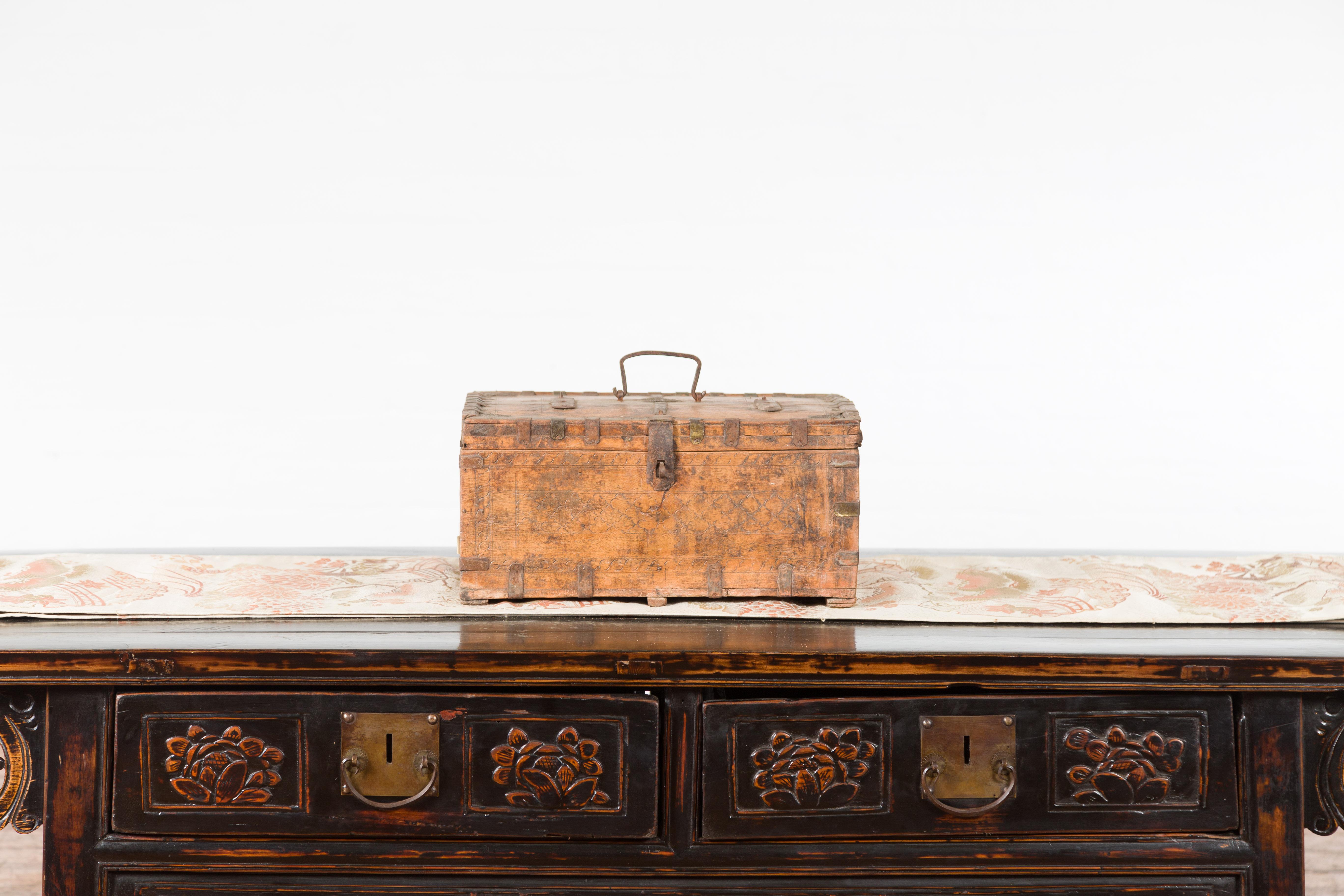 Boîte rustique indienne en bois du XIXe siècle, à l'aspect joliment patiné, avec des détails en fer et des motifs sculptés. Créée en Inde au XIXe siècle, cette boîte en bois présente un couvercle rectangulaire qui s'ouvre à moitié pour révéler un