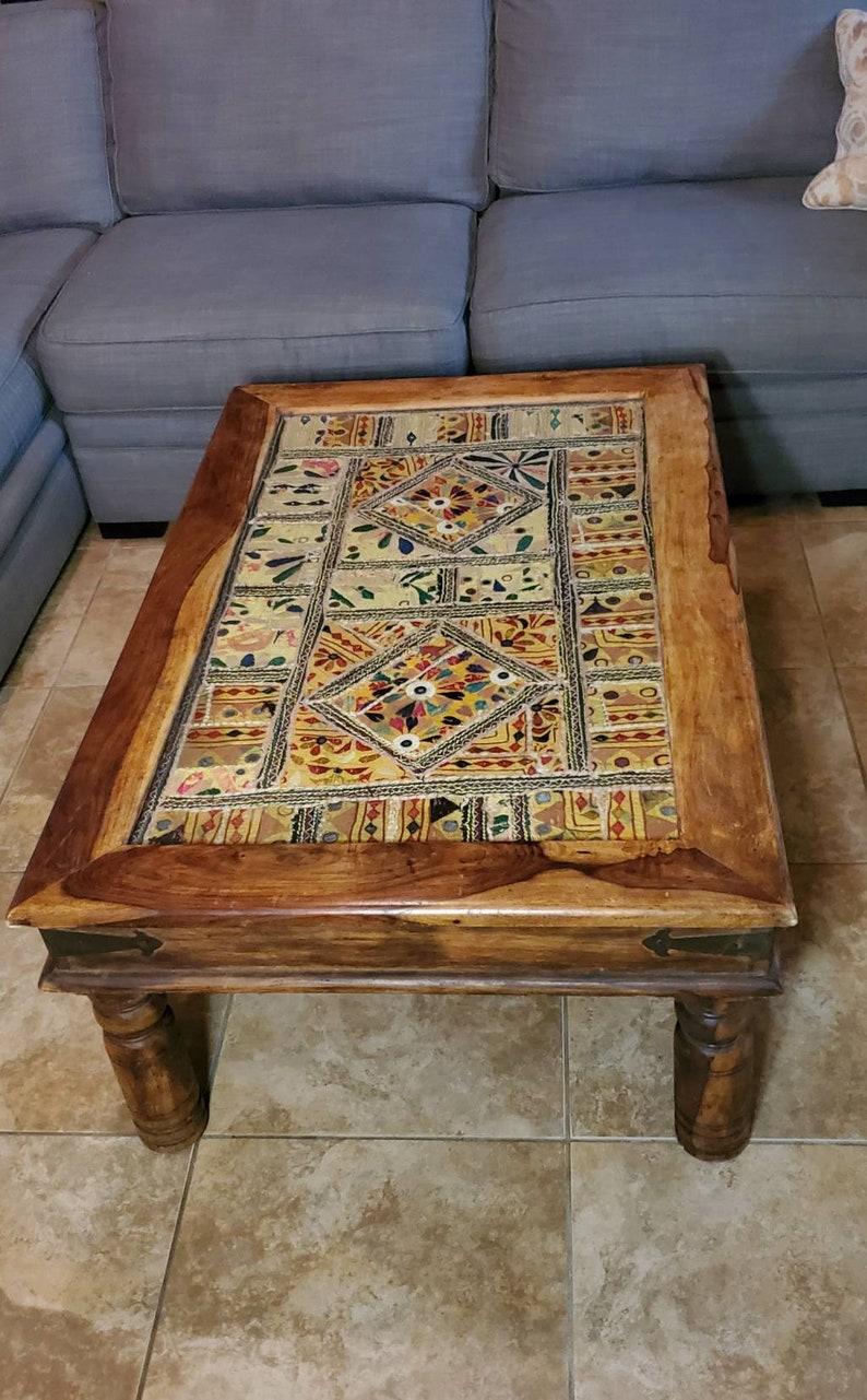 A truly unique rustic solid wood glass top tapestry coffee table from India. Featuring a stunning and vibrant antique Indian embroidered tapestry, under a protective glass insert tabletop, wooden table frame with beautiful color and grain pattern,