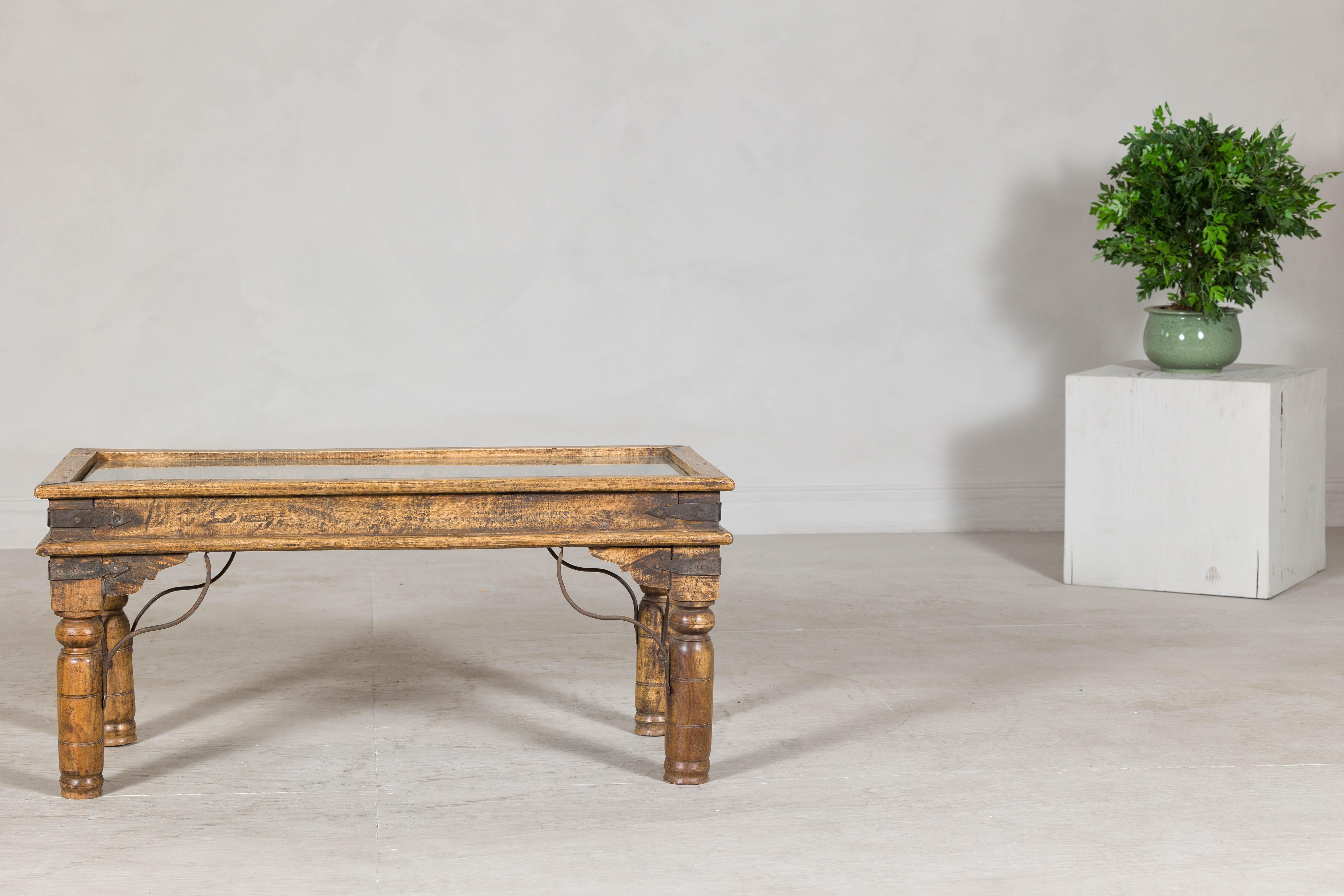 This vintage coffee table from India pairs rugged architectural salvage with refined craftsmanship to striking effect. The focal point of the design is an antique iron window grate, repurposed as the central feature beneath a custom glass top. The