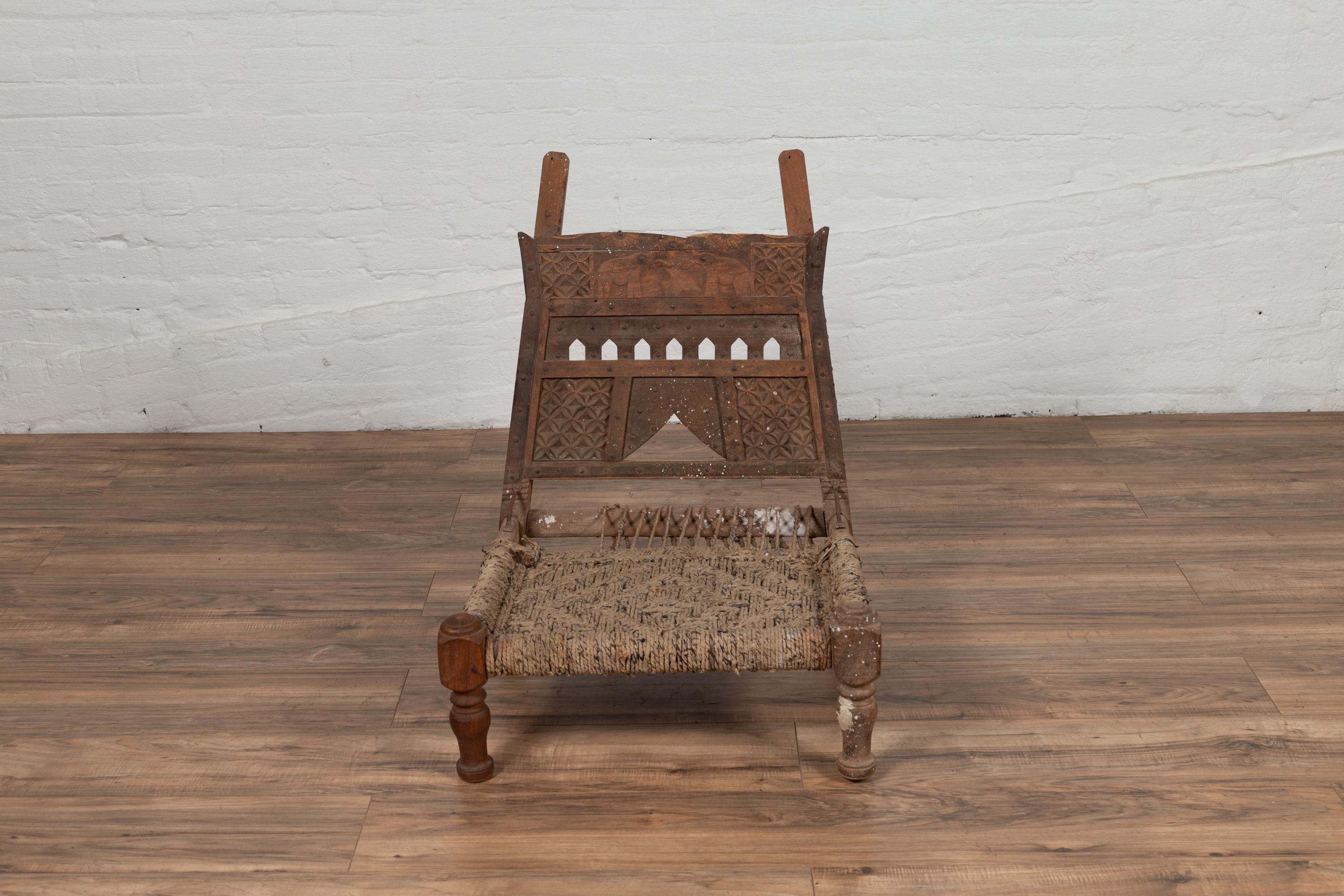 An antique Indian rustic low chair from the 19th century with rope accents and elephant motifs. Imbued with the rustic spirit of 19th-century India, this low chair serves as a tangible remnant of history, perfect for adding a touch of authenticity