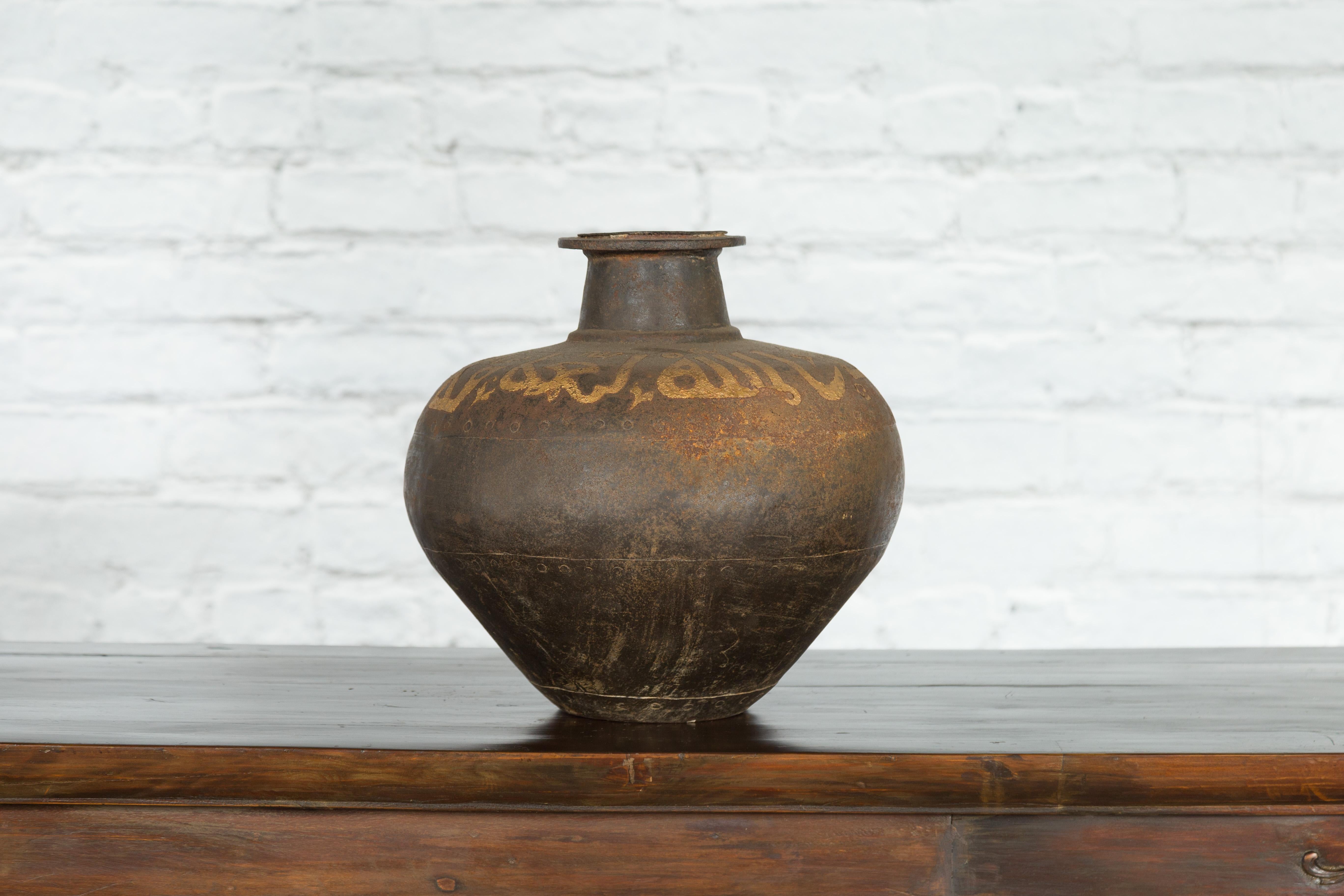 A vintage Indian vase from the mid-20th century, with gilded calligraphy and distressed appearance. Created in India during the midcentury period, this rustic vase attracts our attention with its tapered lines and weathered patina. A narrow neck