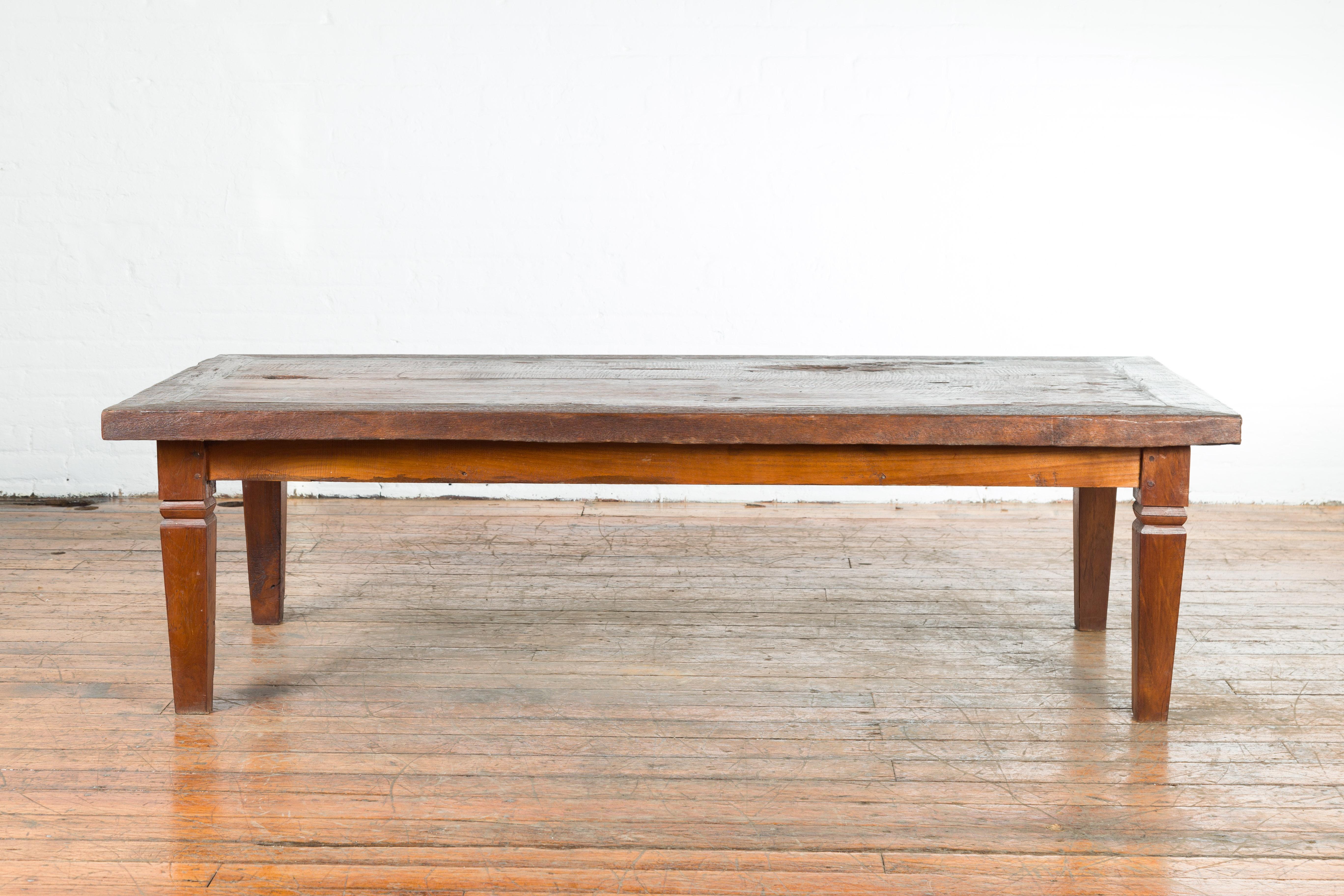 A rustic Indonesian wooden coffee table from the 19th century, with tapered legs. Created in Indonesia during the 19th century, this coffee table draws our attention with its rustic planked top boasting a nicely weathered appearance, sitting above