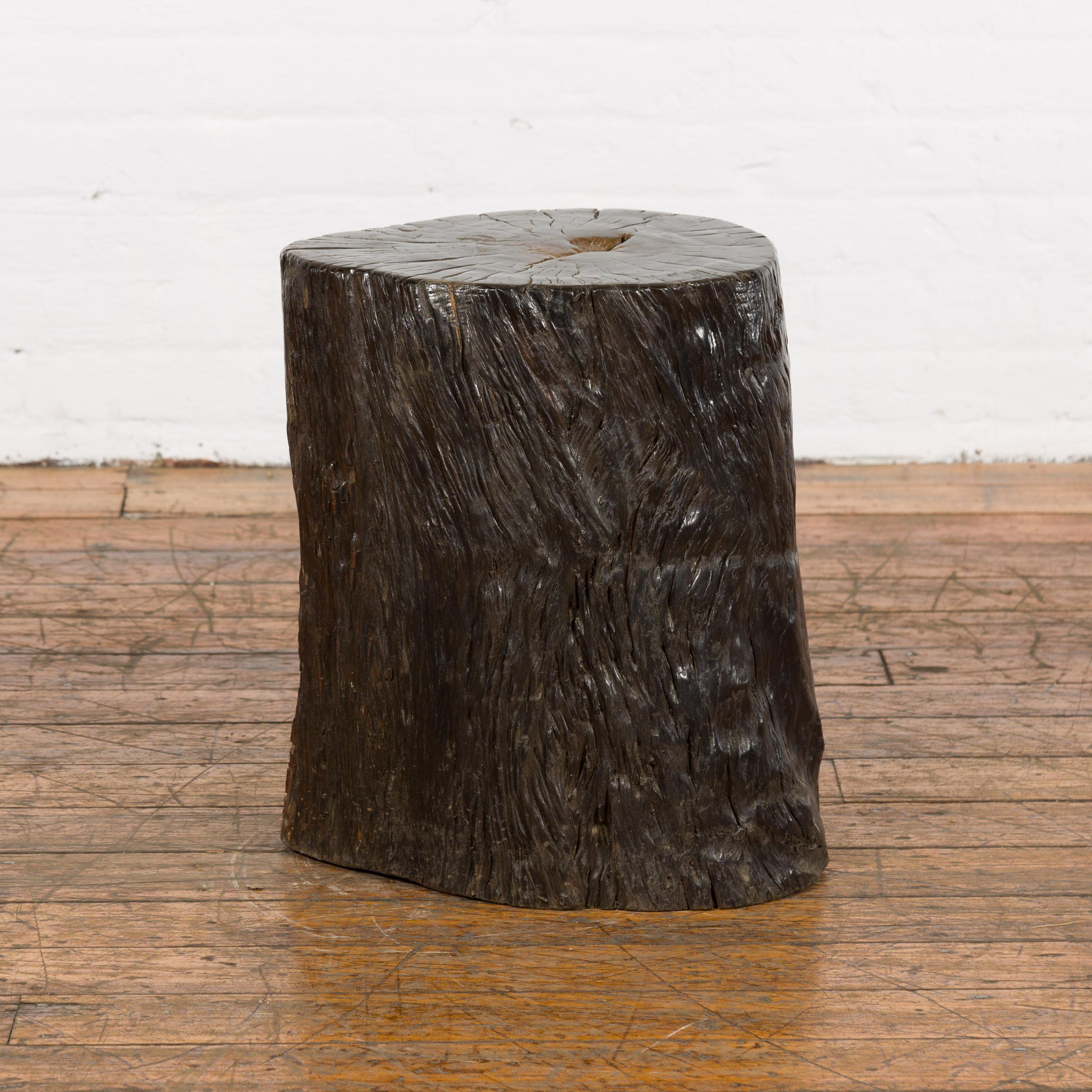 An antique Indonesian petrified wood tree stump drinks table or stool with black color. Bring a slice of Indonesian antiquity into your space with this petrified wood tree stump. Doubling as both a stool and a drinks table, this piece exudes a