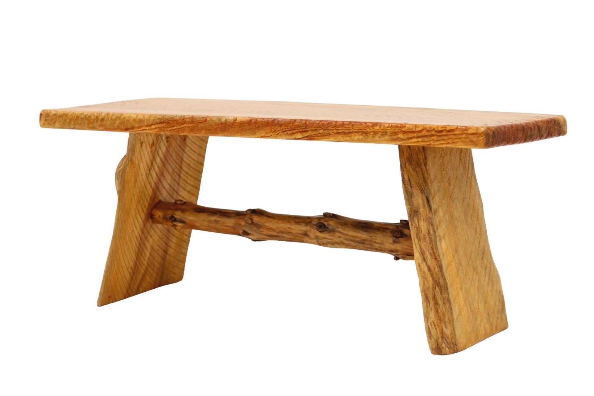 A rustic bench made from solid pine. Three pieces of richly grained plank wood have a natural live edge. Underneath a pine branch serves as a stretcher.
