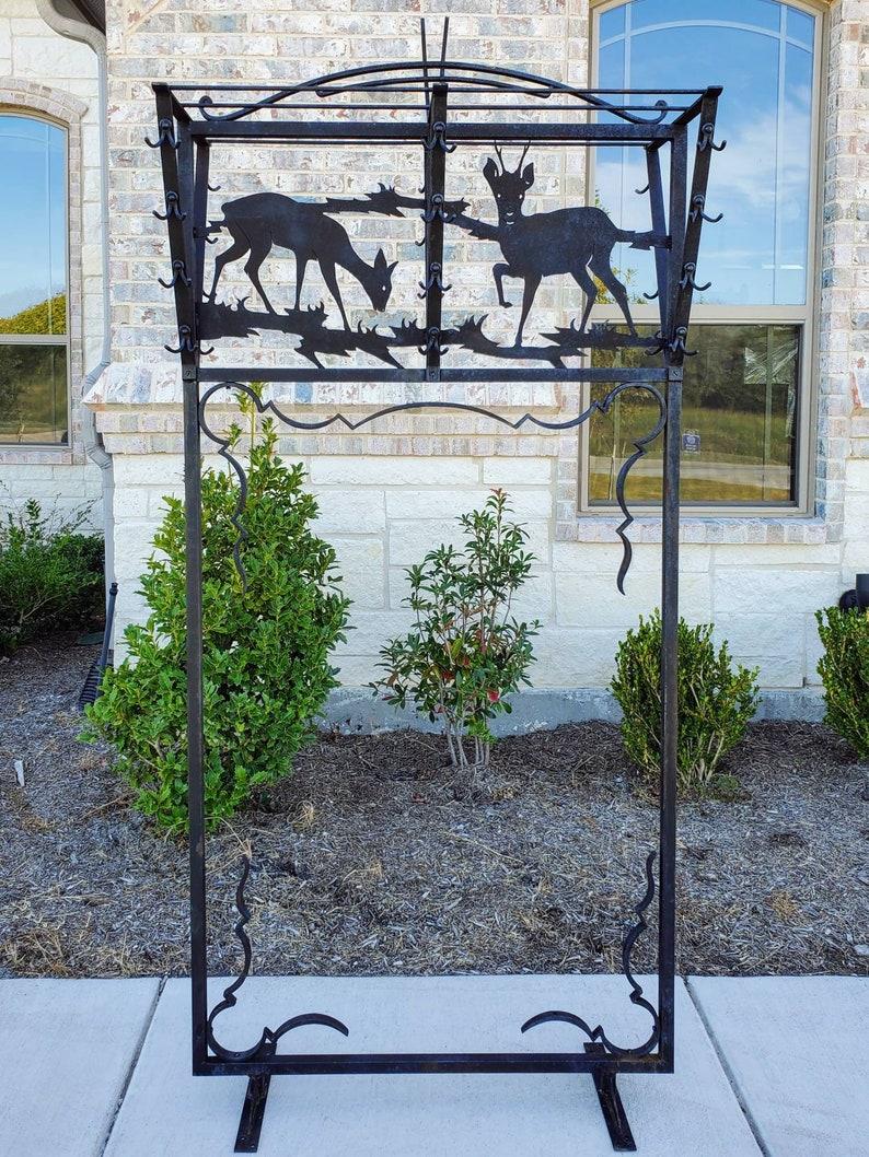 A monumental rustic Spanish style black hand forged wrought iron and hammered metal hall tree / coat hanger / room divider screen / freestanding rack. Dual sided, having a naturalistic figural deer scene, featuring standing stag with four point