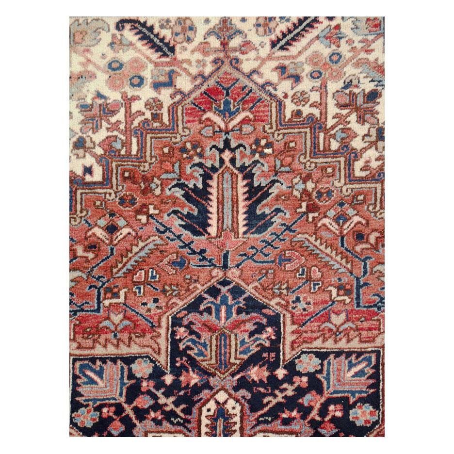 A vintage Persian Heriz room size rug handmade during the mid-20th century. The rustic design consists of a dark blue medallion and border with a light red subfield and corner spandrels over an ivory field.

Measures: 8' 4