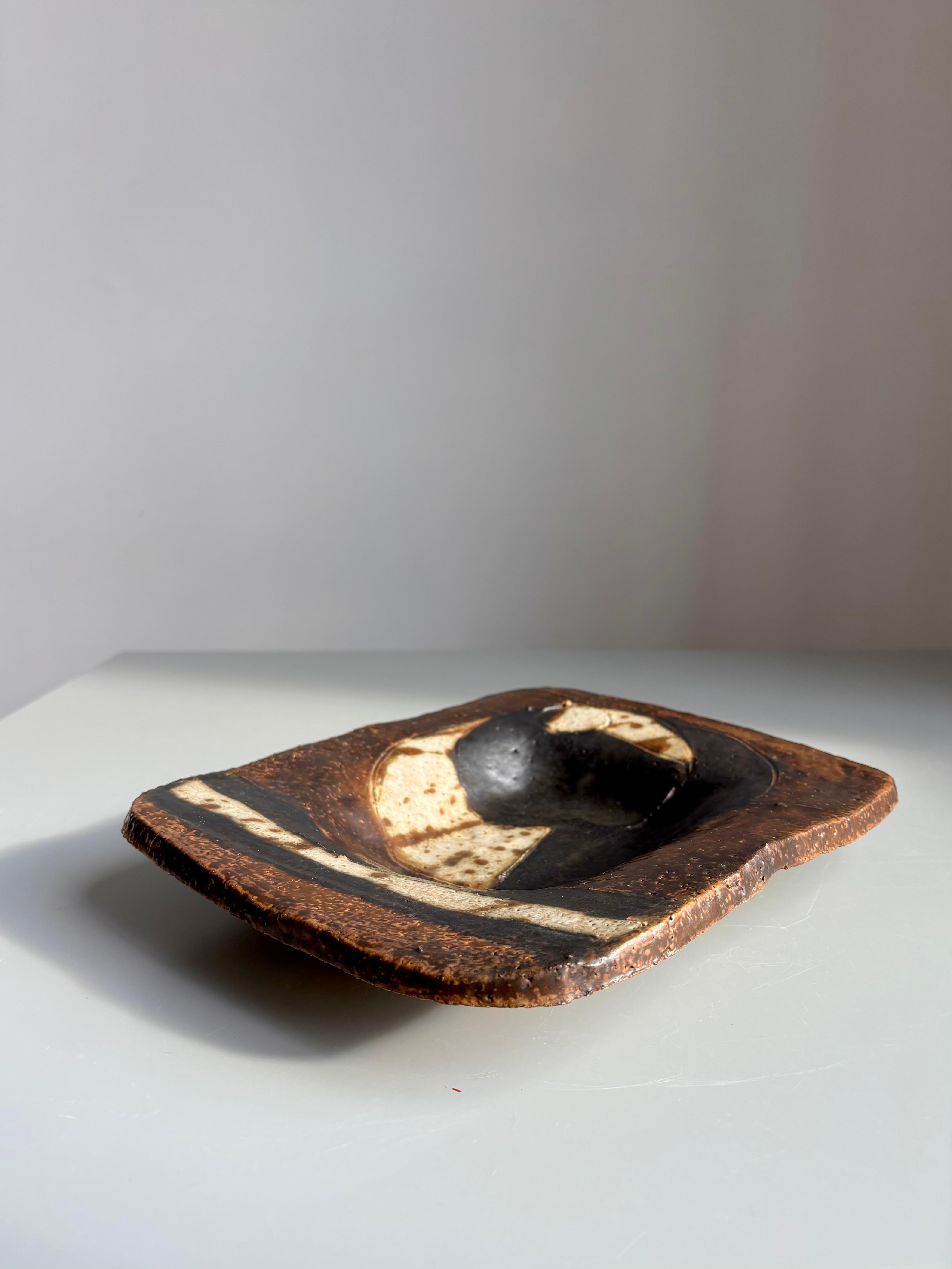 Midcentury modern ceramic artwork to be used as decoration, serveware or wall hanging. Earthcolored matte glaze in modernist abstract lines and shapes. Cream, brown and black colors. 
Signed and dated on the back. 
Beautiful vintage condition.