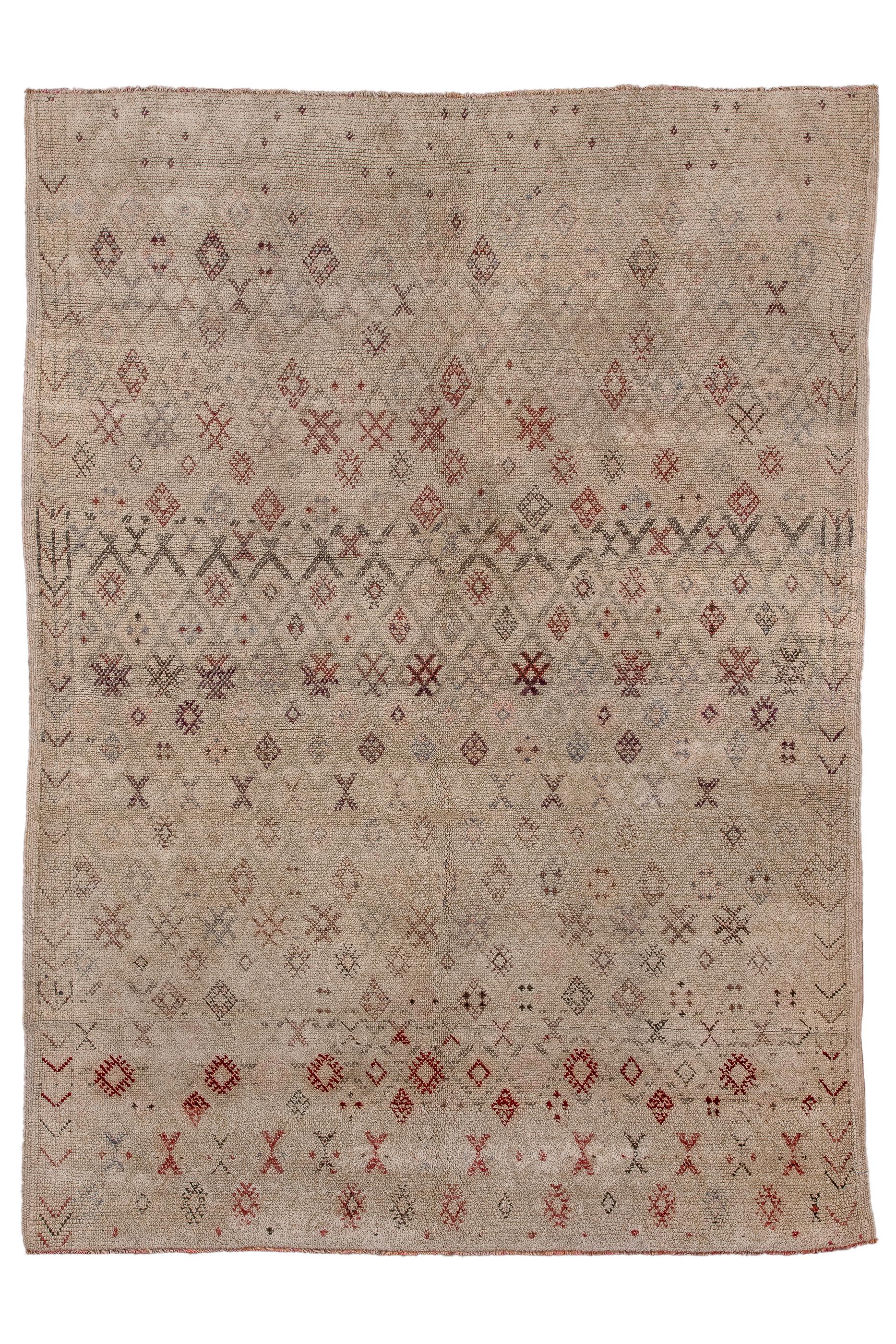 This large rustic Moroccan rug shows a tan field overlaid with a lozenge trellis allover pattern with various geometric devices, including: X’s, cross hatch tiny lozenges and small lozenges; all in shades of brown, with a few darker horizontal runs.