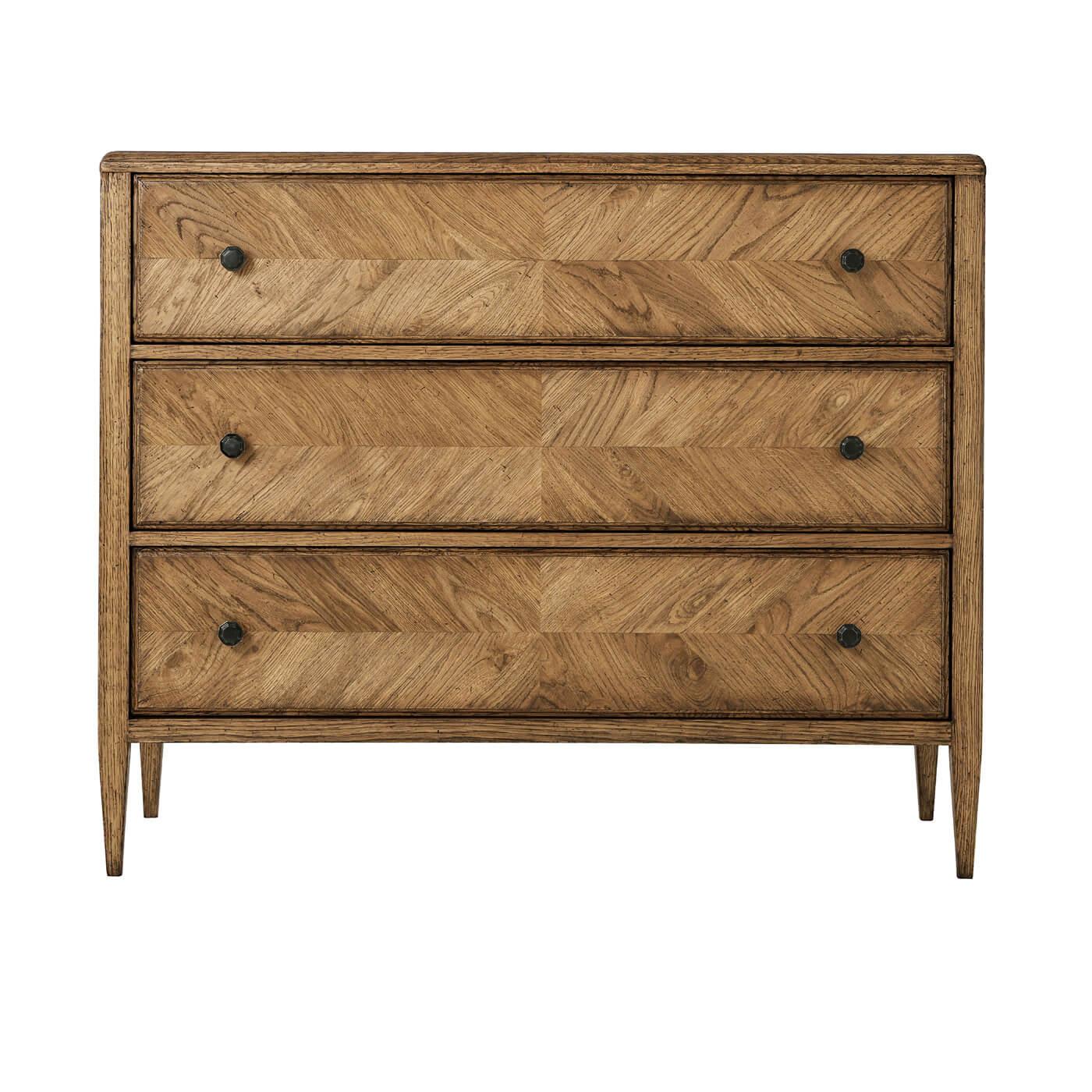 A rustic chest of drawers crafted with light rustic oak. It has a mirrored herringbone oak parquetry design with three oak-sculptured drawers accented with Verde Bronze finished knobs and beautifully tapered oak legs.

Dimensions: 46