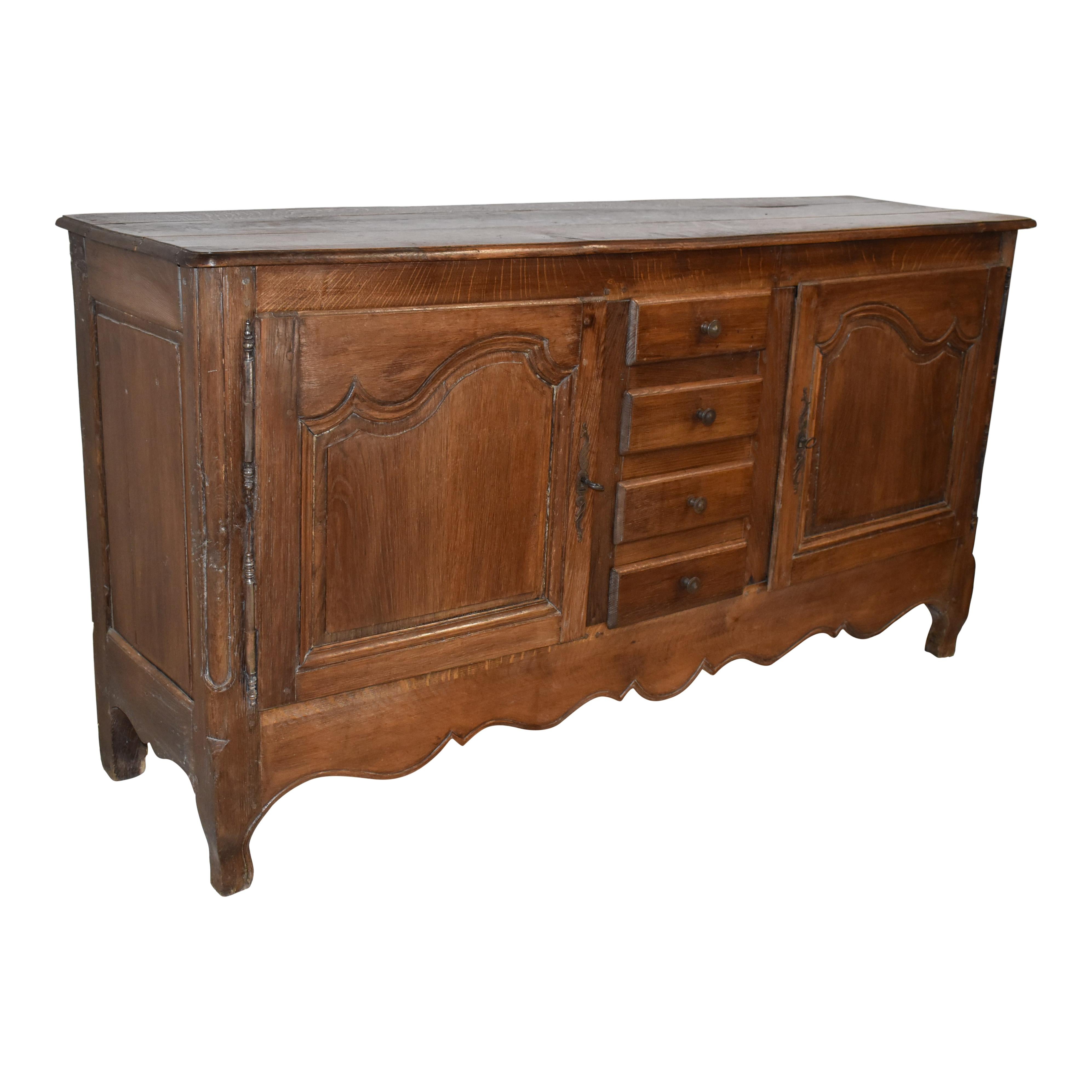 Featuring solid oak construction from the late-19th century, this six-foot sideboard pairs rustic appeal and soft, graceful lines. The graceful lines are evident in the raised panel doors that are scalloped at the top; rounded front edges on the top
