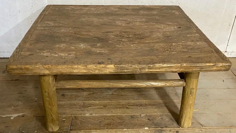 The rustic almost square country style Asian elm wood coffee table has rounded legs and stretchers with solid pegged construction. The plank top is secured by breadboard ends. The rusticity of the table lends itself to informal living indoors or on