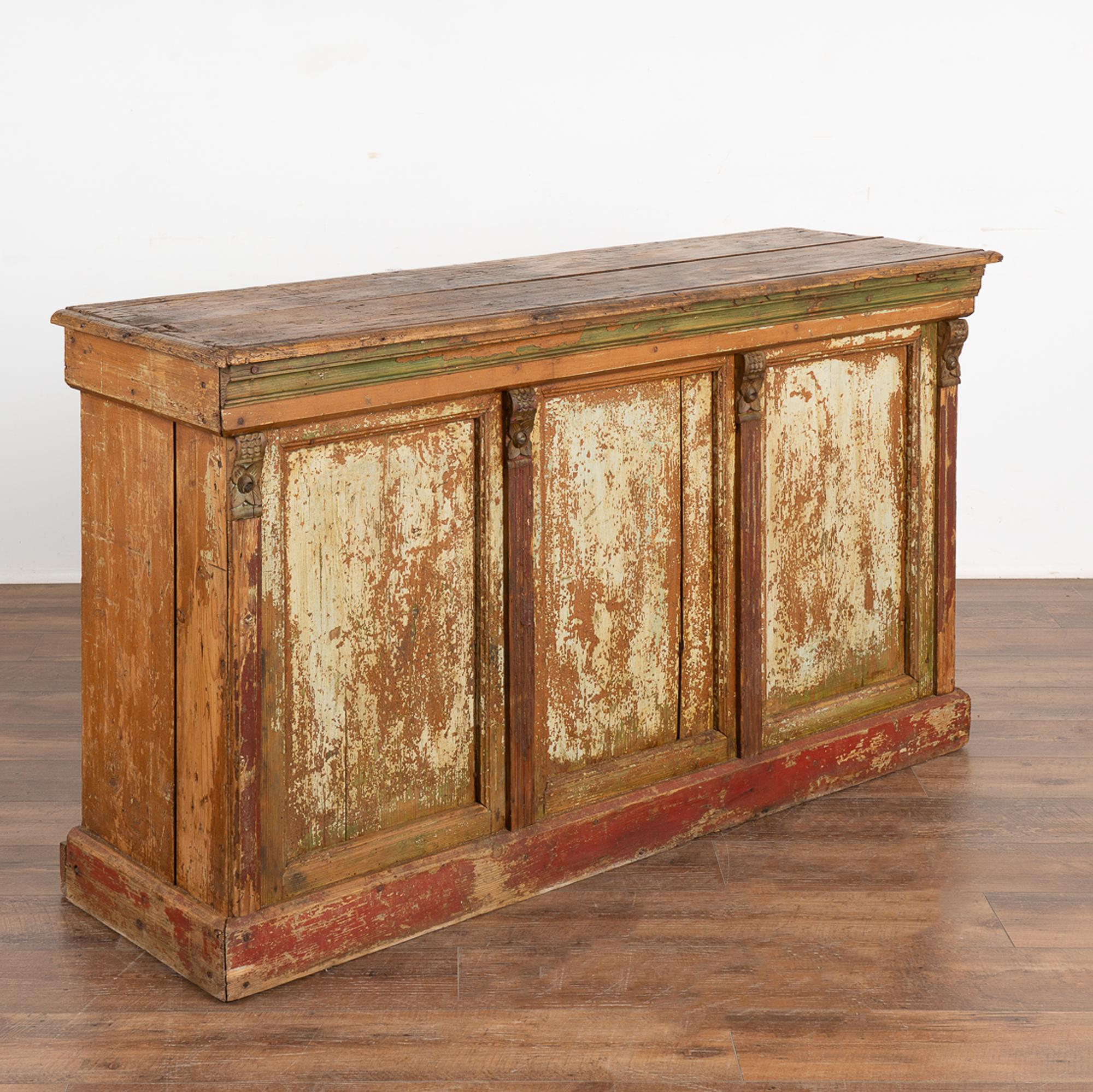 Antique 5' shop counter with original residual paint over natural pine. Yellow, green and brown paint are still visible on the open storage side, while the opposite enclosed counter has red and green trim with white on the panel doors. All the paint