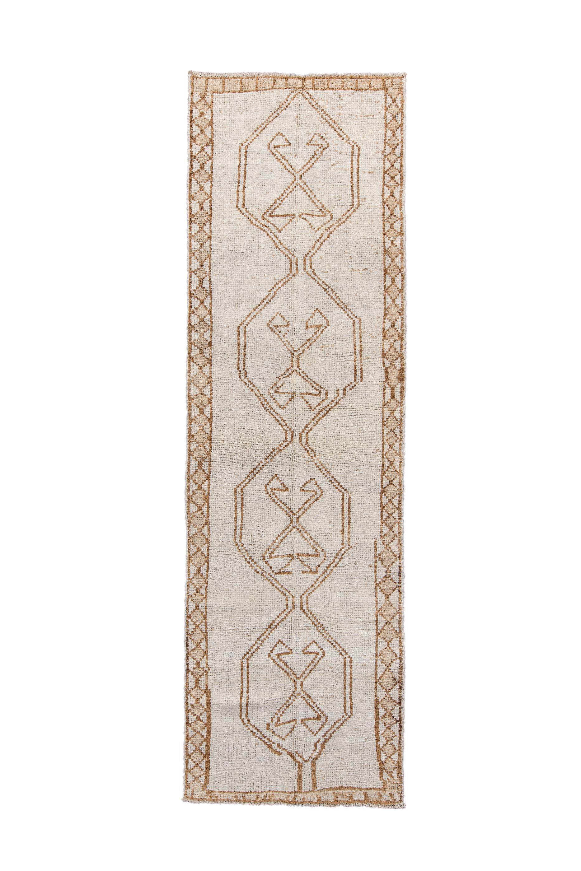 This definitely rustic kenare (runner) shows a lightly abrashed cream/sand open field centred by an equal ly open, tonally en suite pole medallion composed of four connected hexagons with quadruple ram’s horn  inner motives. The very narrow border