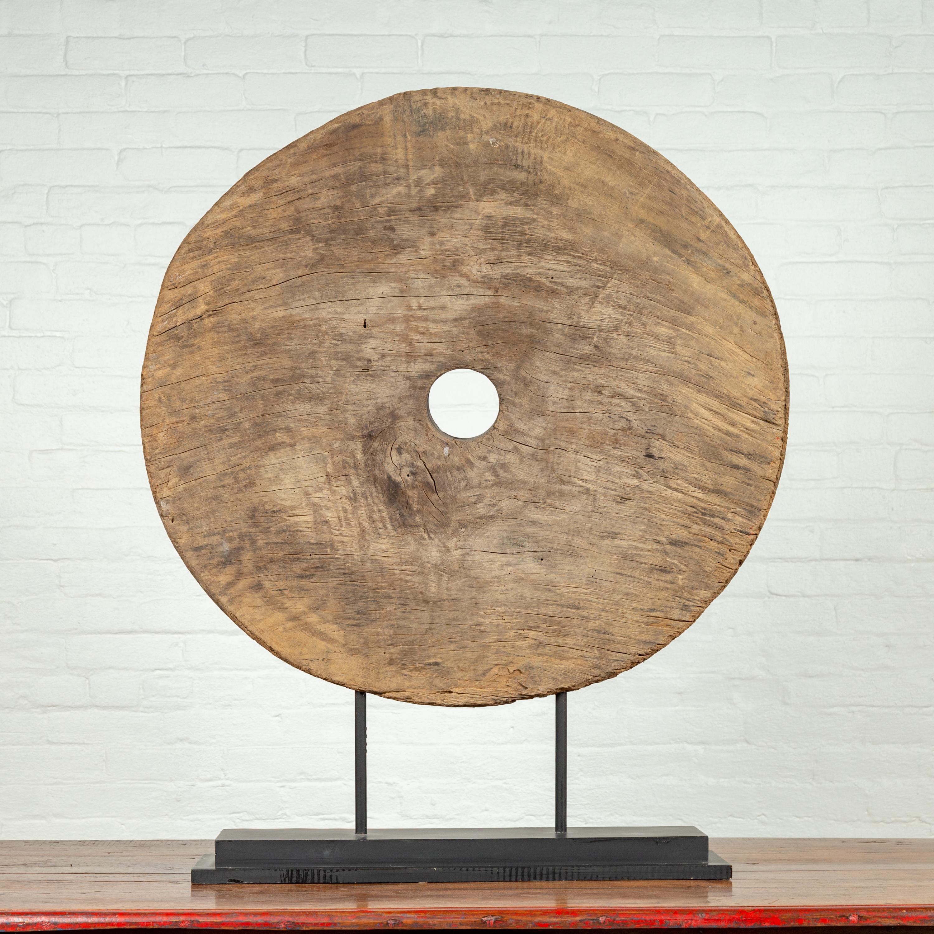 A rustic Thai 19th century ox cart wooden wheel mounted on a custom made black wooden stand. Born in Thailand during the 19th century, this handmade wheel is pierced in its center with a circular hole reserved for the axle tree. The wheel showcases