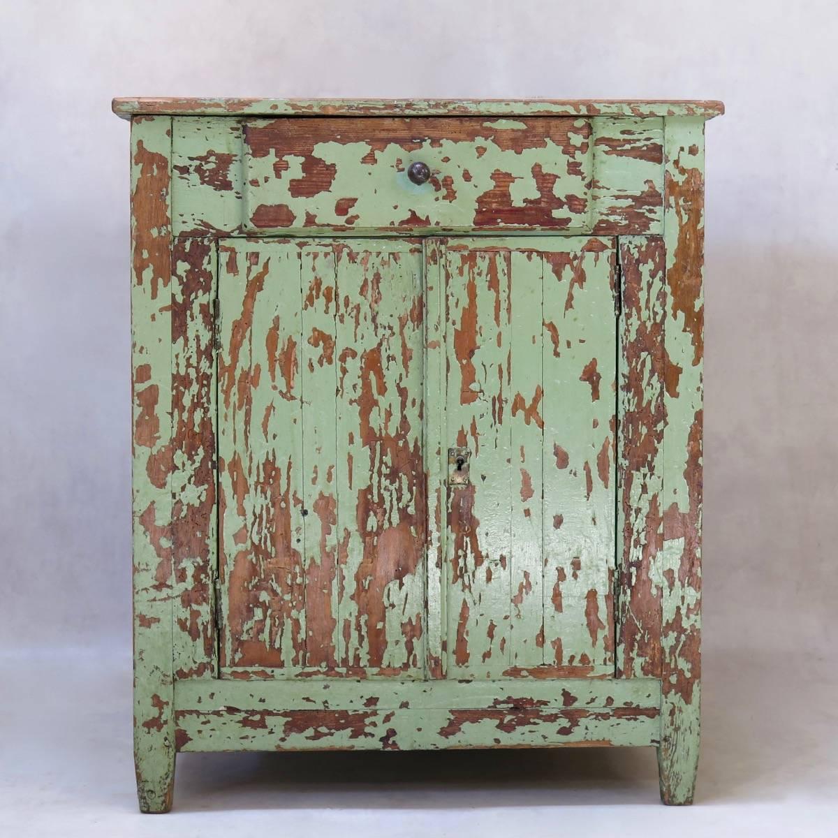 Charmante armoire en bois de pin, dont la peinture verte brillante s'écaille. Les deux portes s'ouvrent sur des étagères (assez profondes). Petit tiroir sous le plateau. Monté sur des pieds courts et légèrement effilés.