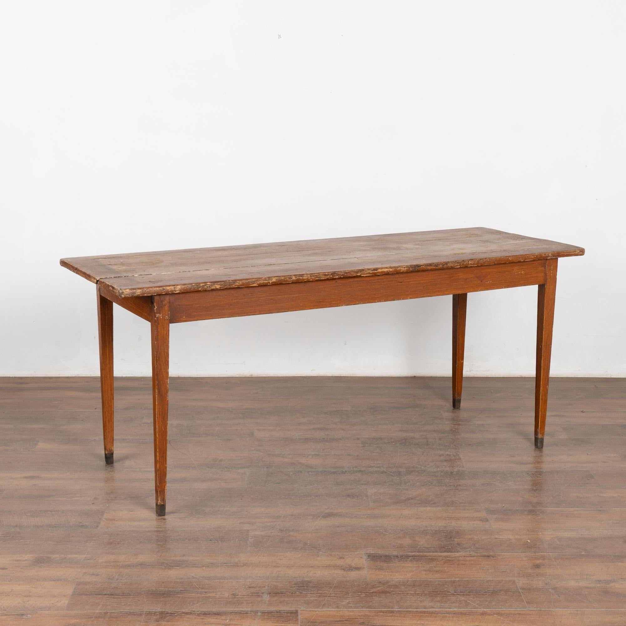 This old farm table with tapered legs has a worn appeal reflected in the original brown faux wood finish which was a traditional folk art style of the era. Black paint is seen at the feet.
Note the scratches, dings, cracks and stains all seen in the