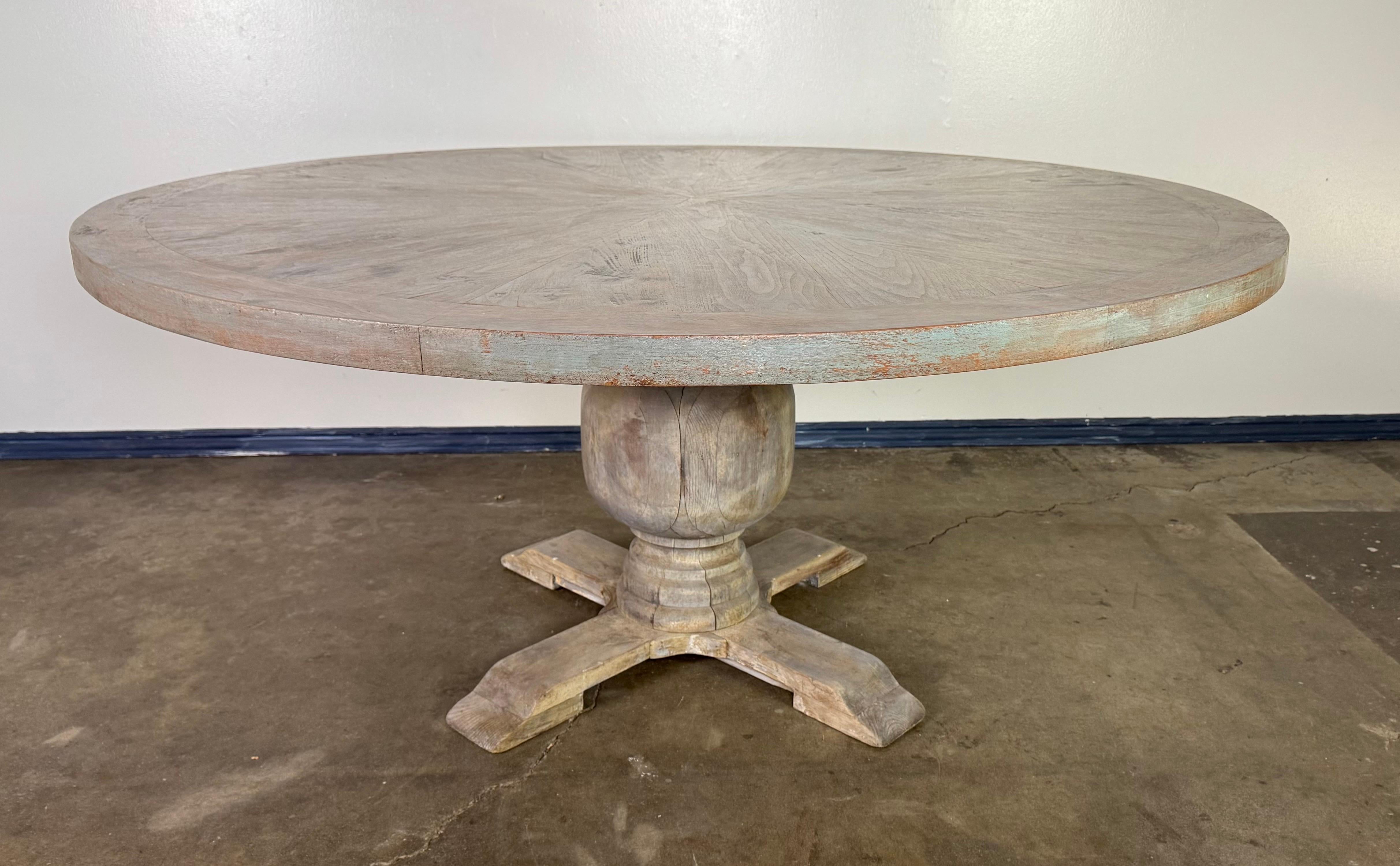 Il s'agit d'un guéridon rustique peint à l'esthétique ferme et vintage. Le plateau de la table ronde présente une finition vieillie qui révèle des touches de bleu doux et de légères nuances rougeâtres, ce qui lui confère un caractère joliment usé