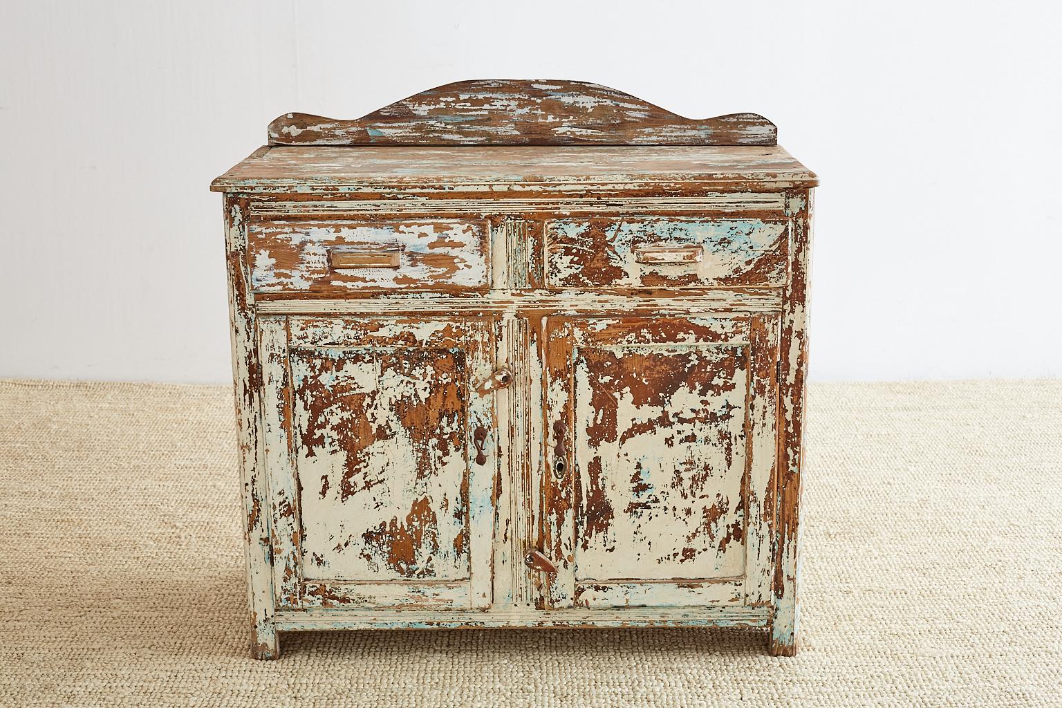 Rustic and primitive painted pine server or sideboard featuring a scraped down distressed finish. Fronted by two drawers and two doors with a backsplash on the top. Remnants of white and blue paint visible combined with the natural pine patina