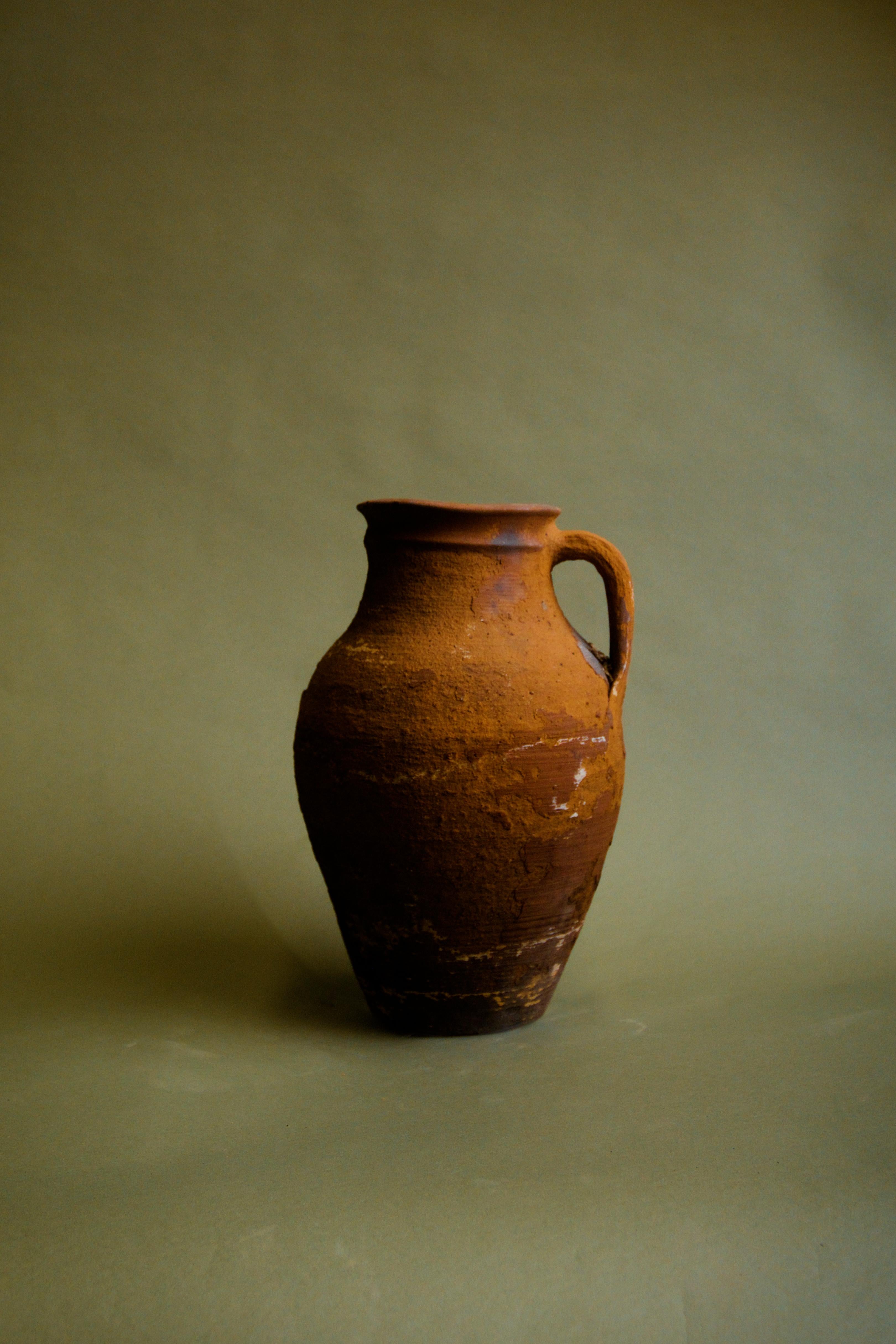 Entra nel fascino dell'eredità turca con questa brocca di terracotta dalla patina rustica, un pezzo splendidamente invecchiato che un tempo serviva come pratico contenitore d'acqua nelle case anatoliche. 

Realizzata a mano in argilla con metodi