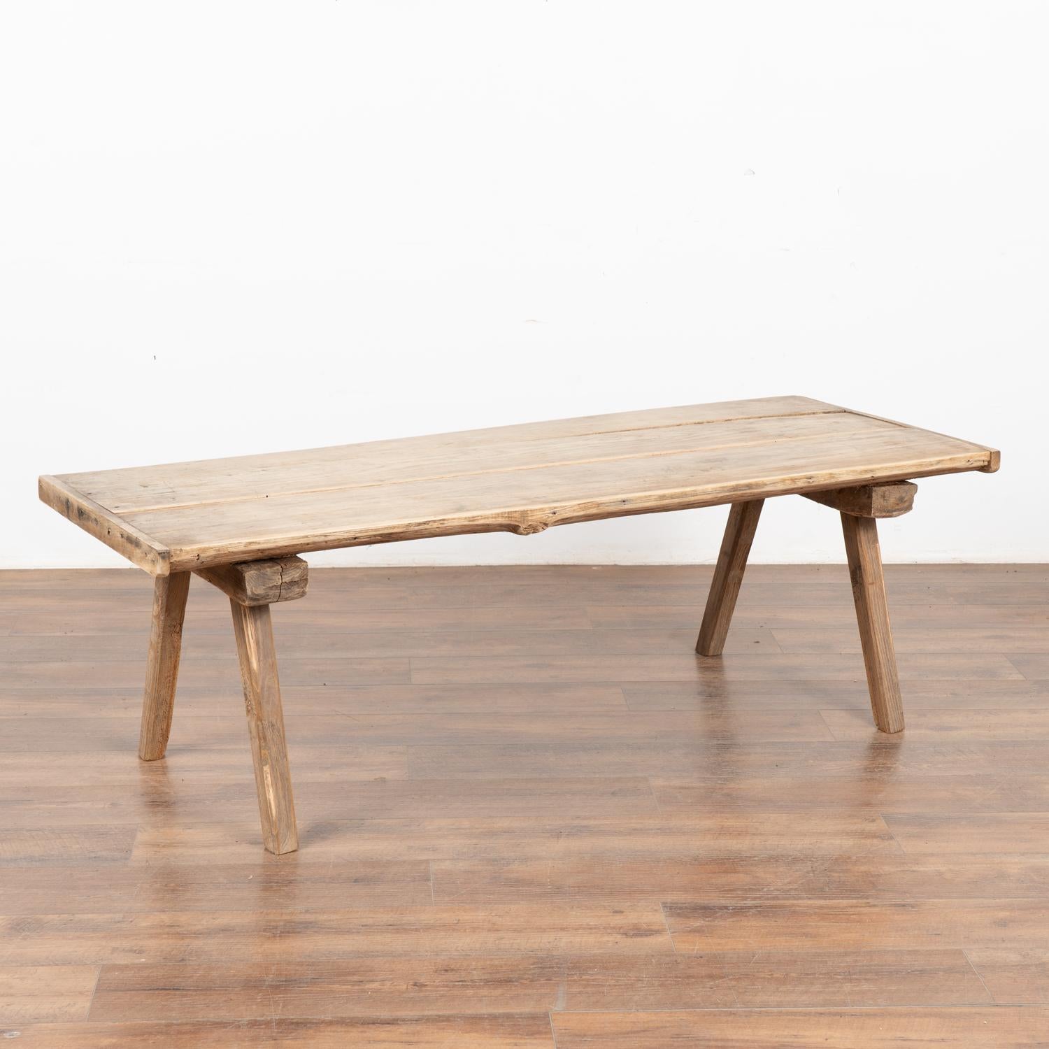 The appeal of this coffee table comes from the rustic wood top that originally served as a work table and rests on original thick peg legs. 
The many scratches, nicks, gouges, stains, old cracks and imperfections that all combine to build the depth
