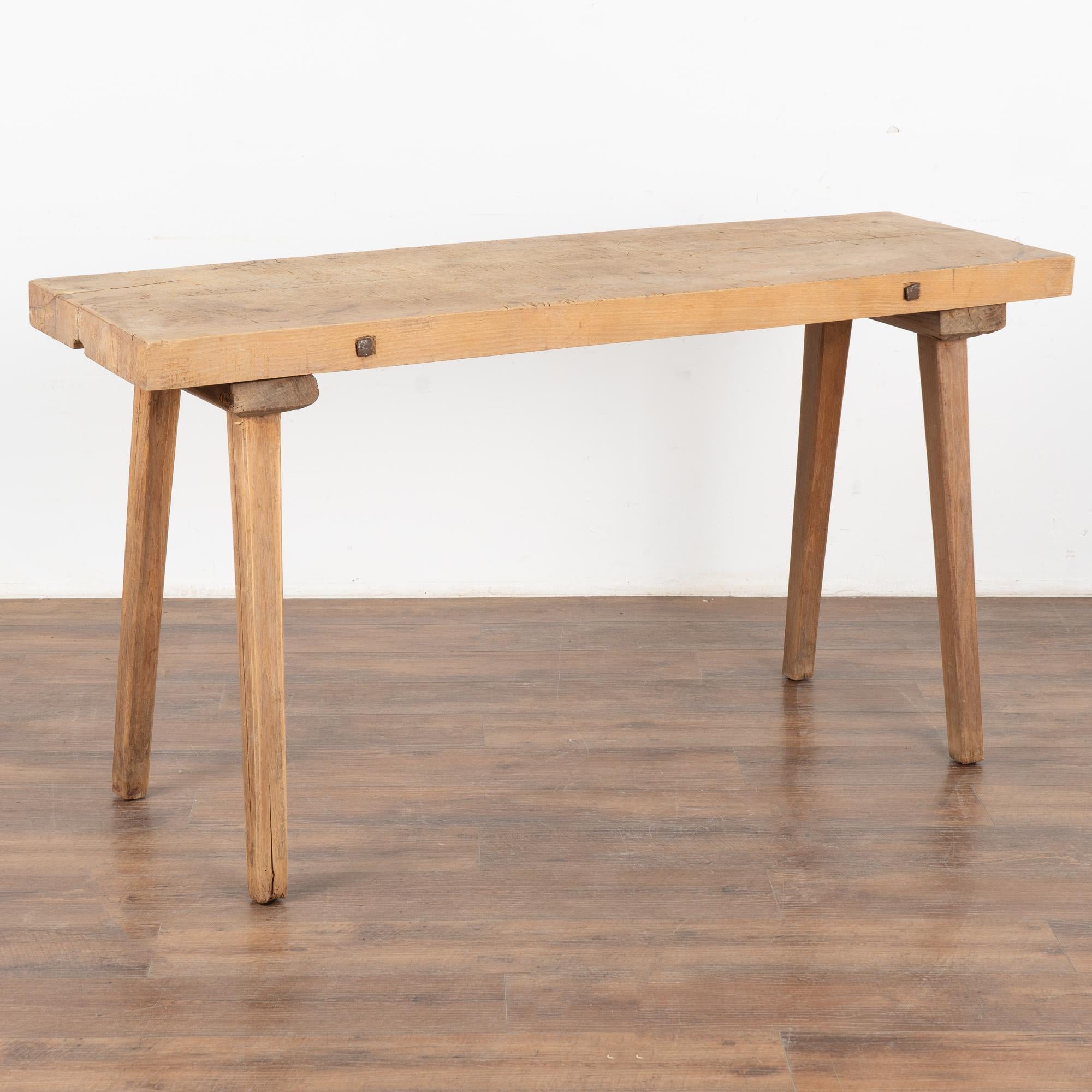 This 5' rustic plank top console table with splay peg legs originally served as a work table. Iron bolts along the edge add a slight industrial feel.
The thick top invites one to run fingers along it, while stains, cracks, nicks, and gouges all add