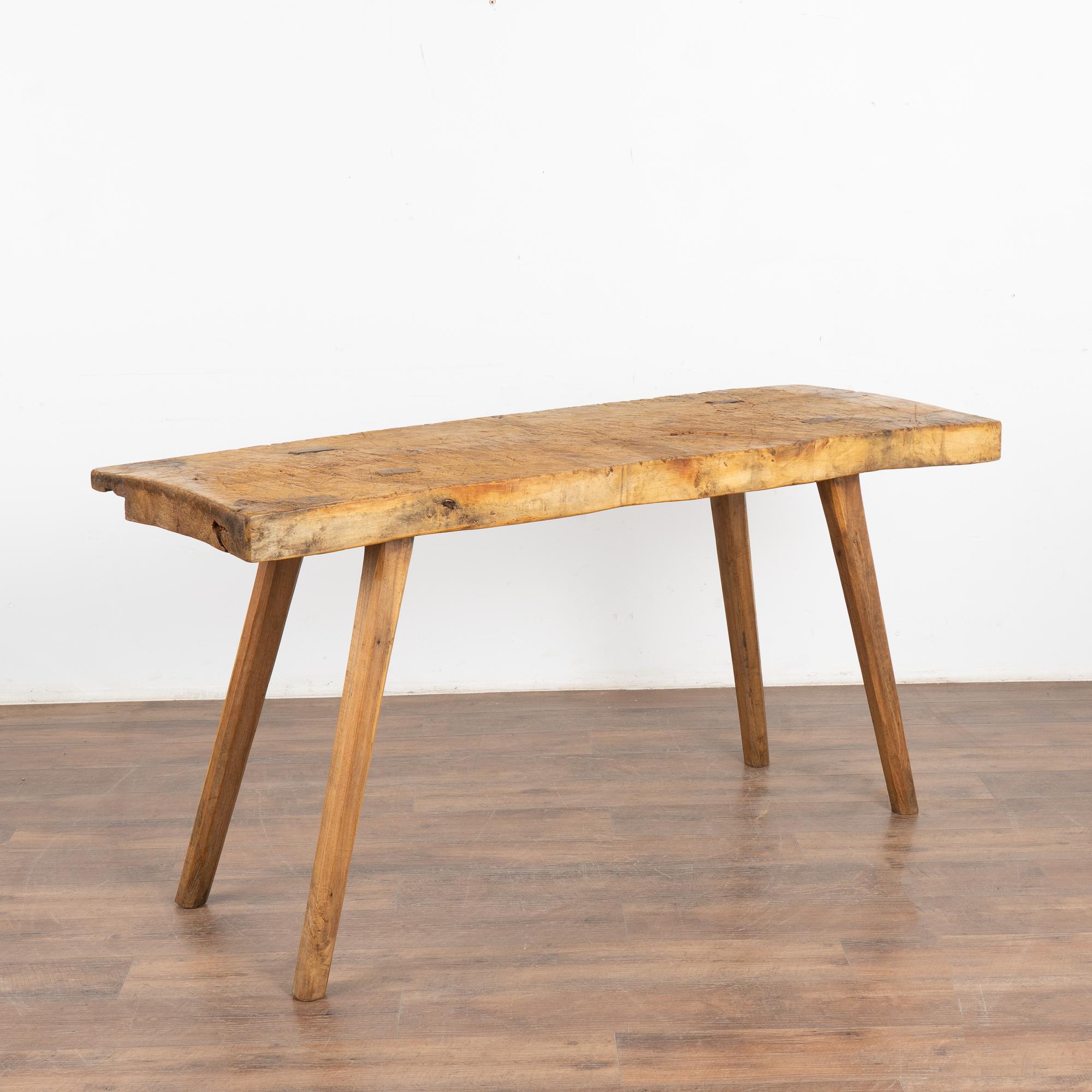 The appeal of this 5.5' long rustic console table comes from the thick hard wood top that originally served as a work table, resting on strong peg legs. 
Note the deep gouges, nicks, old cracks, and stains that all combine to build the vintage
