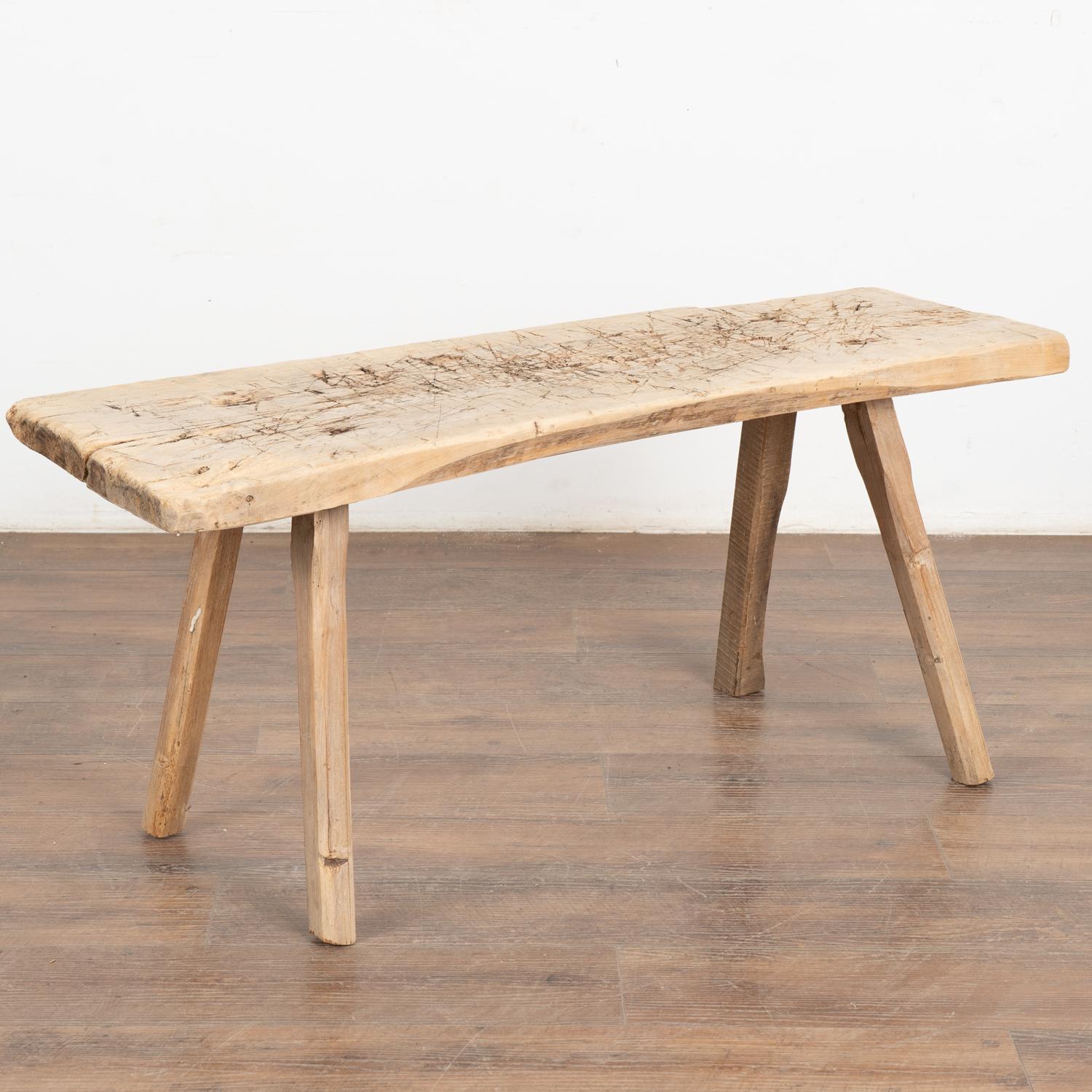The appeal of this rustic bench at just under 4' long comes from the thick hard wood top that originally served as a work table, resting on strong squared peg legs. 
Note the heavy gouges, nicks, old cracks, dried worm holes and stains that all