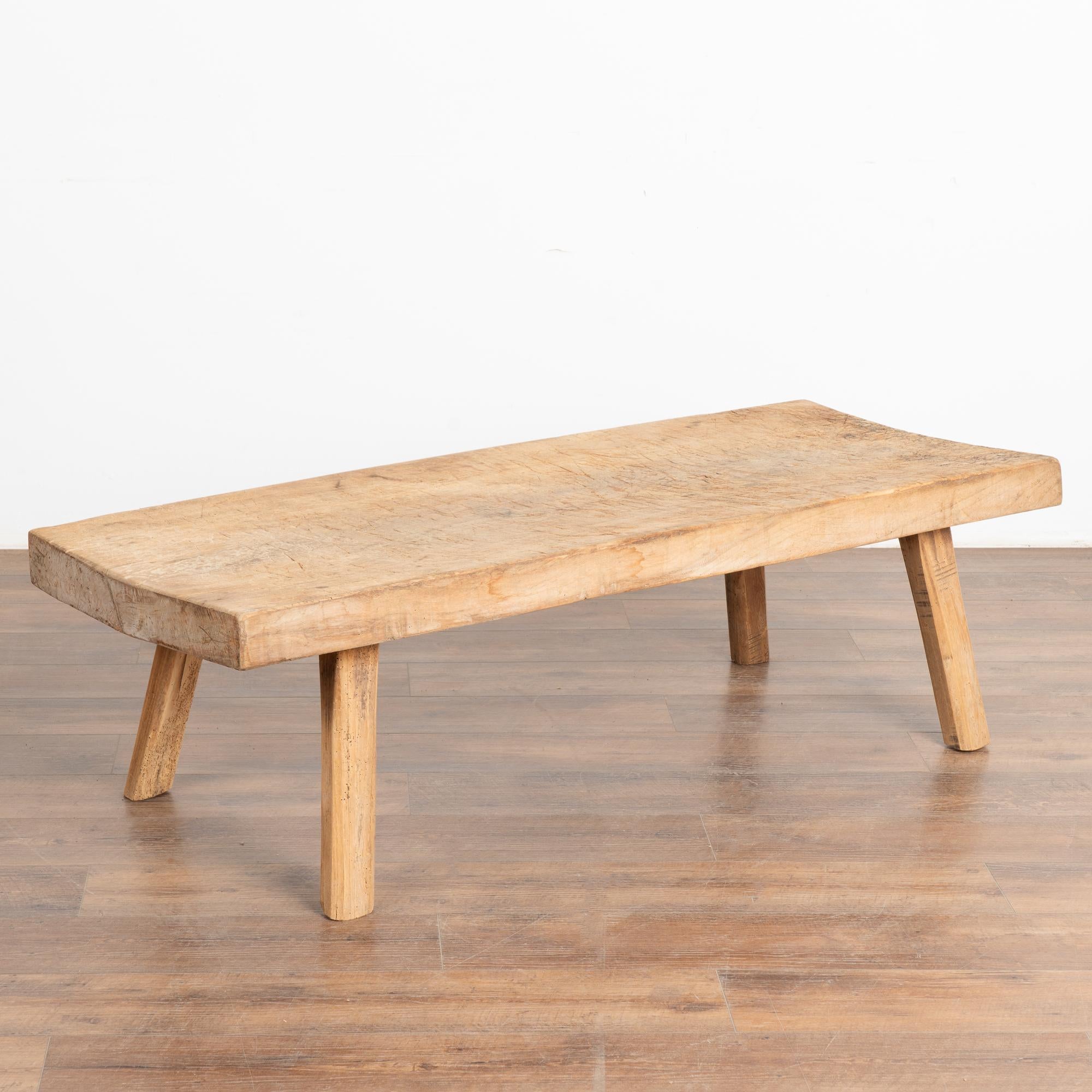 The appeal of this rustic coffee table comes from the thick wood of the top that originally served as a work table. 
Note the gouges, nicks, old cracks and stains that all combine to build the vintage character of this coffee table. 
This table has