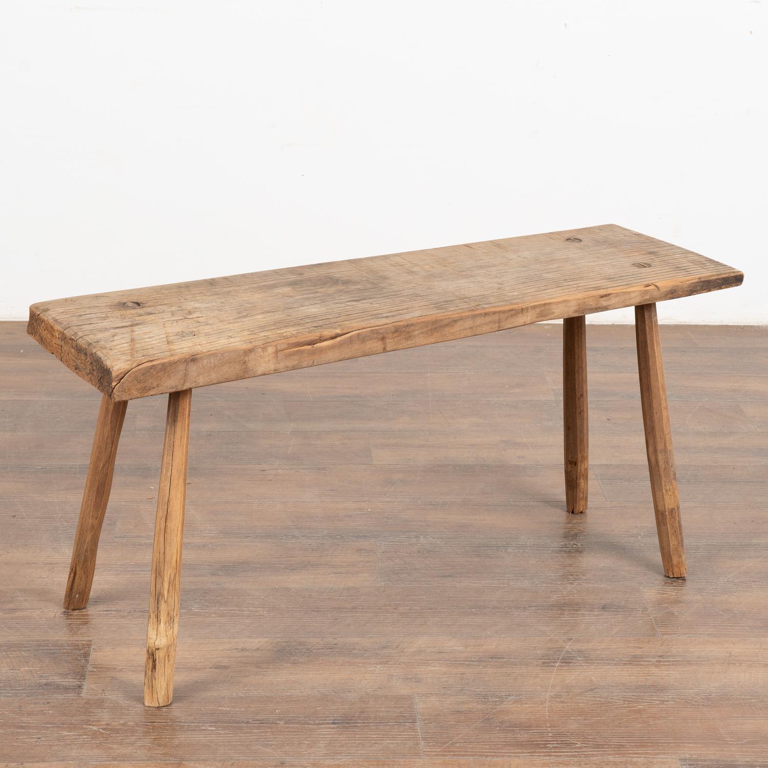 The thick top of this rustic bench is covered in scrapes, gouges, nicks, stains, and old cracks acquired with over 100 years of use. May also serve as a small coffee table.
The top is a single slab of wood with traditional splay peg legs creating