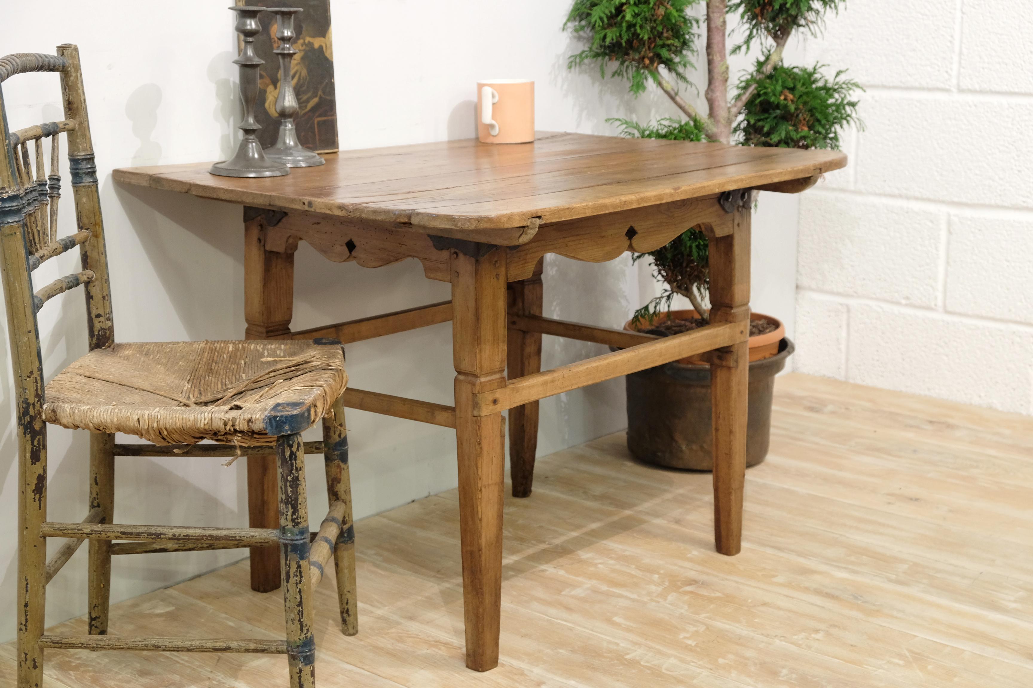 Delightful rustic Spanish side table in pine with a terrific color and patina. Plank top with plenty of characterful wear, hand carved aprons with wrought iron corner braces, tapered legs with box stretchers. Evidence of historic woodworm