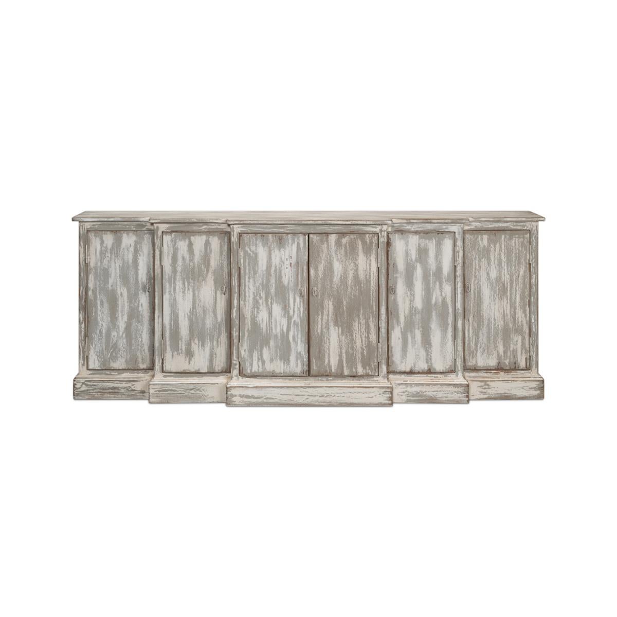 With a heavily distressed and antiqued painted finish. Grey and white color. Made of pine with six paneled doors with a waterfall step back breakfront design. The doors open to a painted interior with shelves. 

With antiqued hardware on a plinth