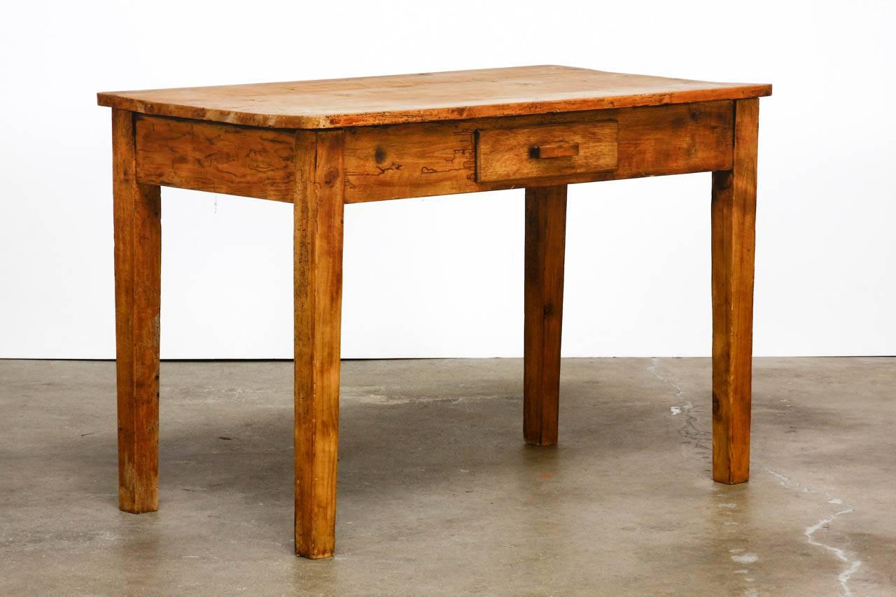Rustic pine work table that could also serve as a diminutive farmhouse desk. The table is fronted by a single drawer and supported by square legs. The pine has a beautifully distressed wax finish with beetle holes, and tons of character.