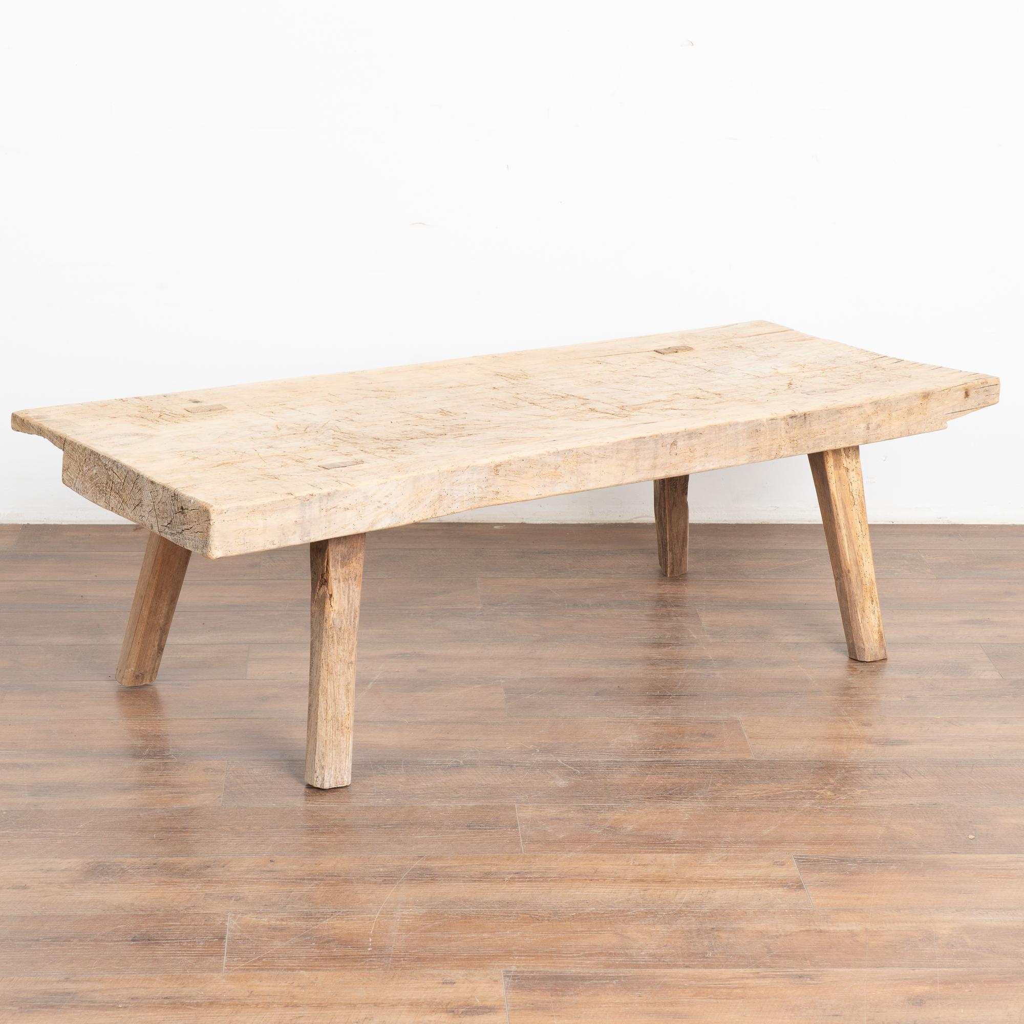 The appeal of this coffee table comes from the rustic wood top that originally served as a work table and rests on original thick peg legs. 
Note the scratches, nicks, gouges, stains and old cracks that all combine to build the depth of character