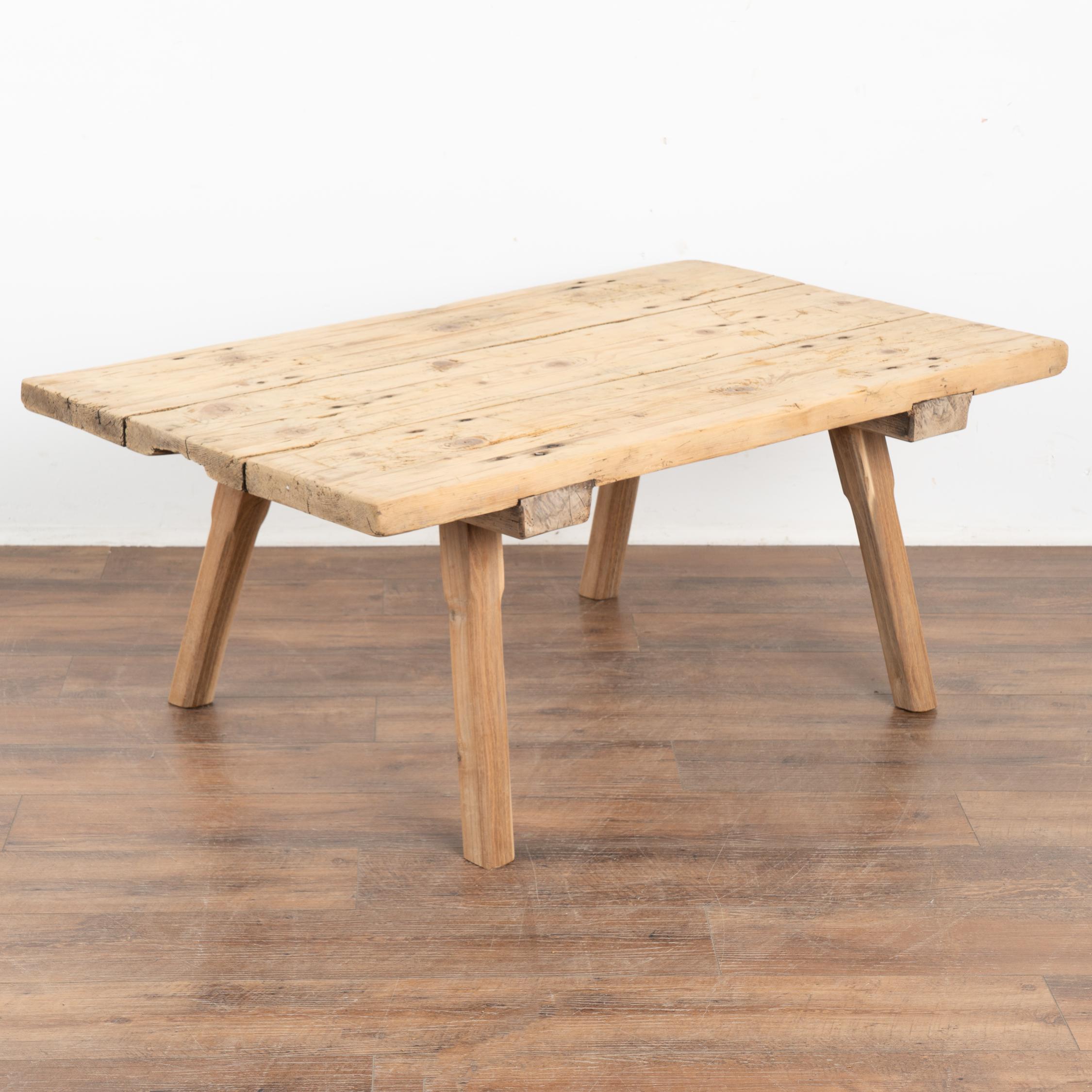 Rustic wood coffee table with squared splay legs and loaded with vintage character.
The thick top is made from three planks which are covered in scrapes, deep gouges, old cracks and stains acquired with over 100 years of use as a work table. Typical
