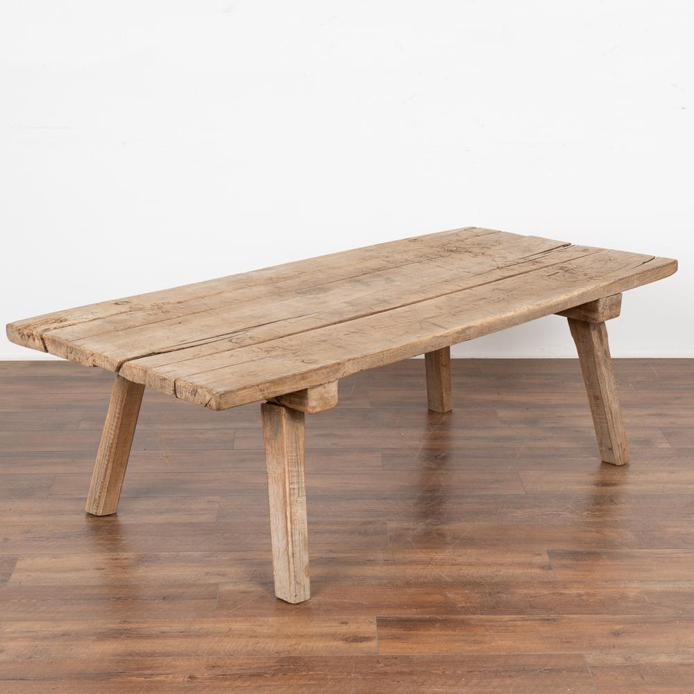 Rustic plank wood coffee table made from three worn planks loaded with vintage character.
The top is filled with old cracks, deep gouges, stains and markings and age-related separation acquired with over 100 years of use as a work table.
The wood