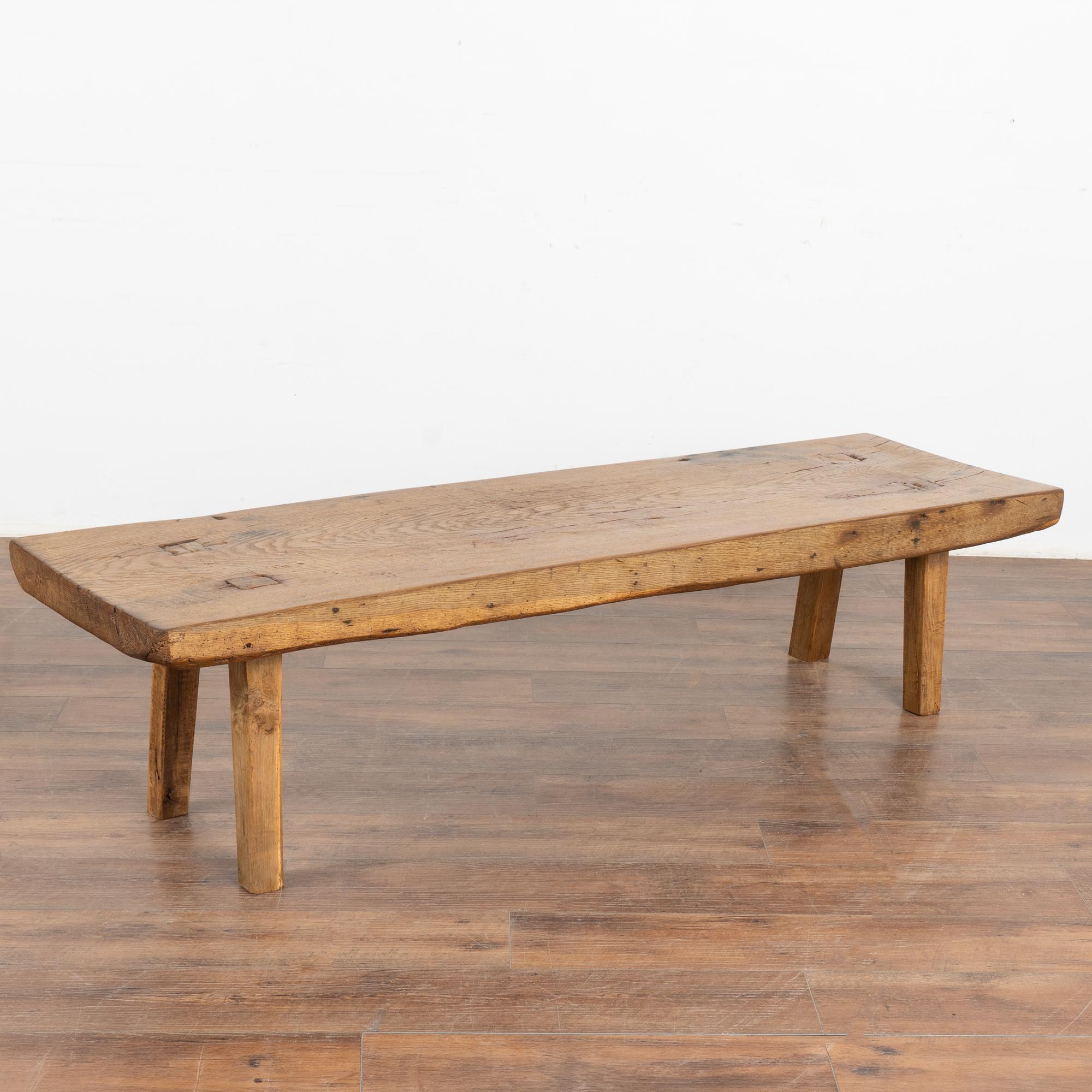 The appeal of this rustic coffee table comes from the thick wood of the top that originally served as a work table.
The slab of wood that serves as the top is impressive and creates the desire to touch it. Note the gouges, stains, scrapes and even