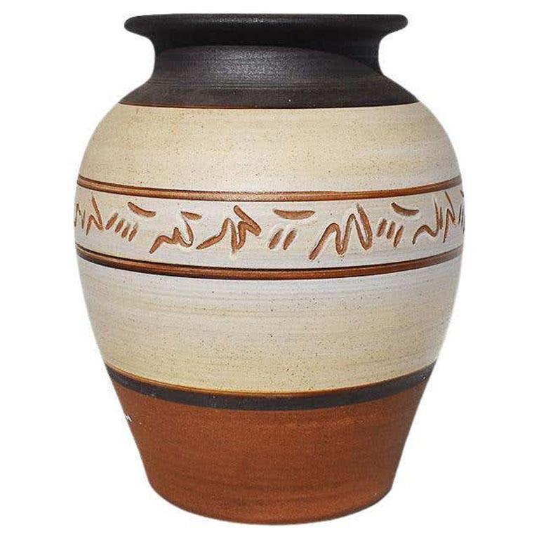 A tall circular rustic hand-thrown ginger jar, planter, or vase in black, brown, and cream. The vase is created from a rough sandy ceramic material. A fluted top is fired in black, and the body is in cream and terracotta orange/brown stripes. The