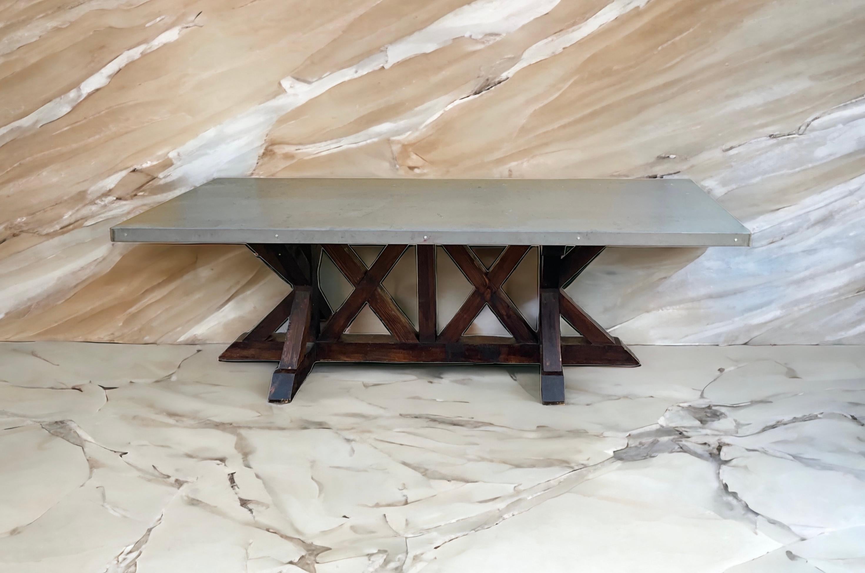 This is just in time for the holidays! It is a large scale primitive farm table with a zinc top and stained oak trestle base. It is less than ten years old and was hand hewn in the United States from responsibly sourced materials. It is in very good