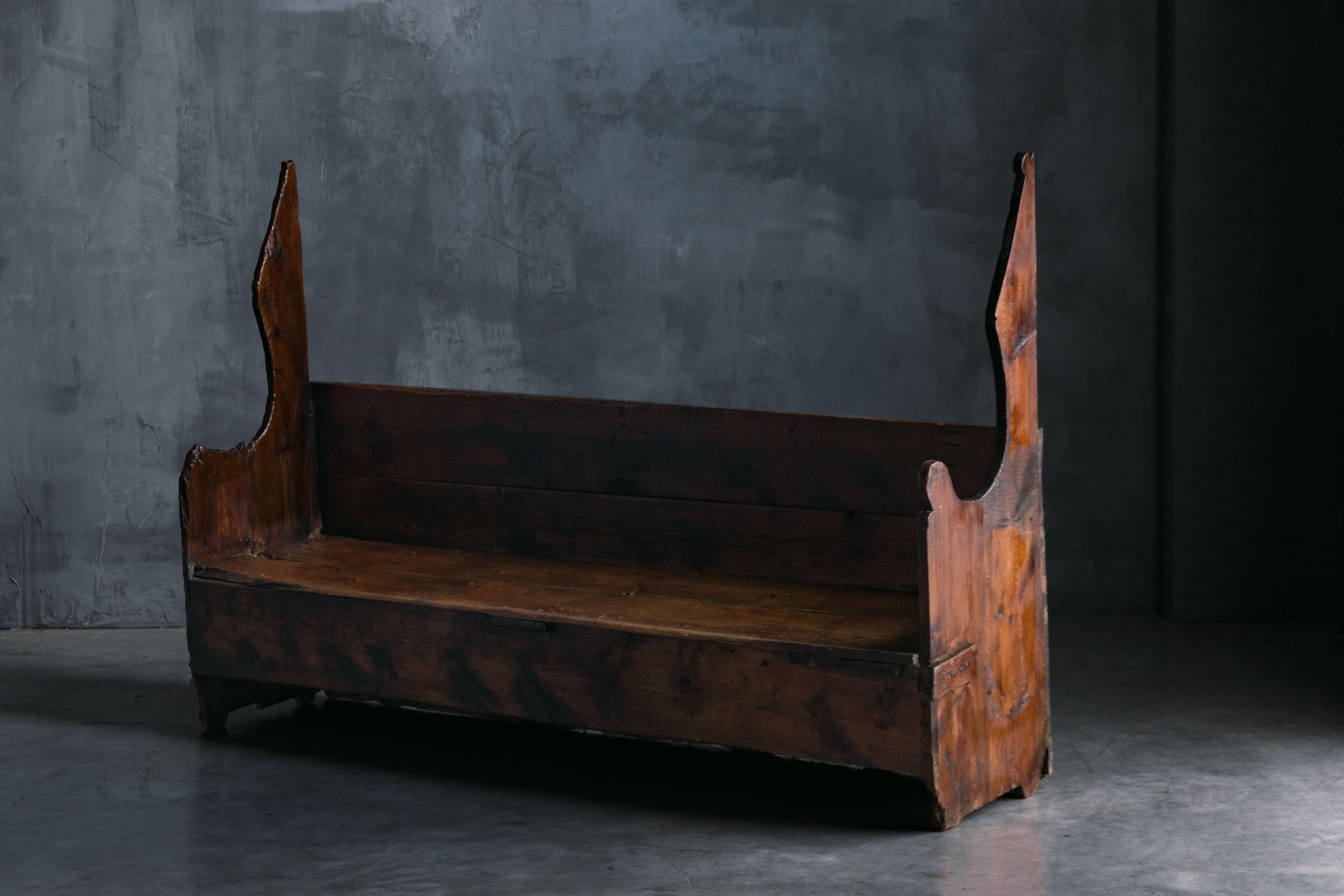 Rustic primitive farmhouse bench dating back to the 1700s from the Catalonia region of Spain. Its structure is crafted from thick, solid wood planks, with a deep, rich patina that has been beautifully worn over centuries of use. The bench is adorned