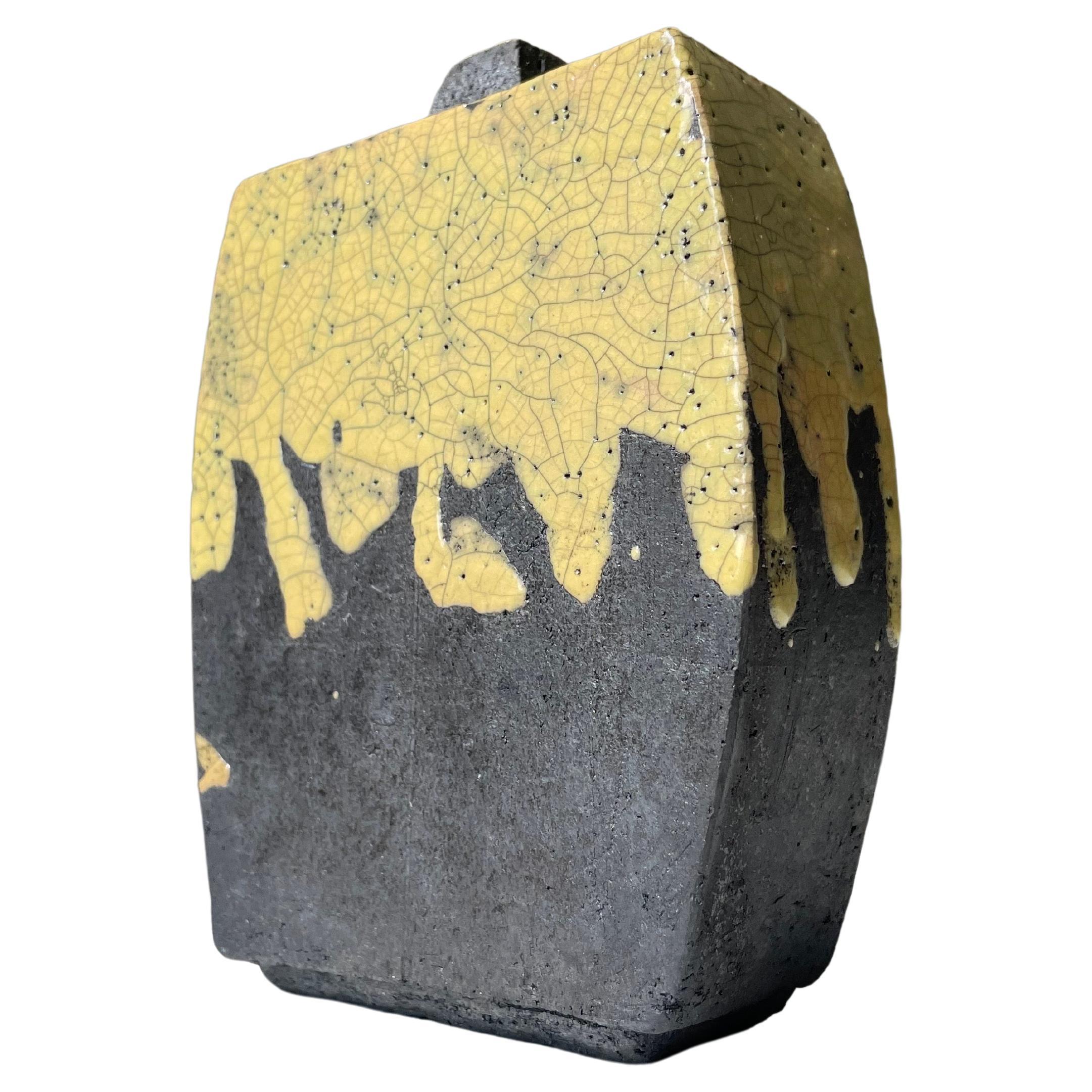 Scandinavian modern Japanese inspired rustic raku ceramic decorative vase. Running yellow crackle glaze over anthracite raw clay. A combination of rounded shapes and straight lines with a short square shaped top partially glazed. Signed under base.