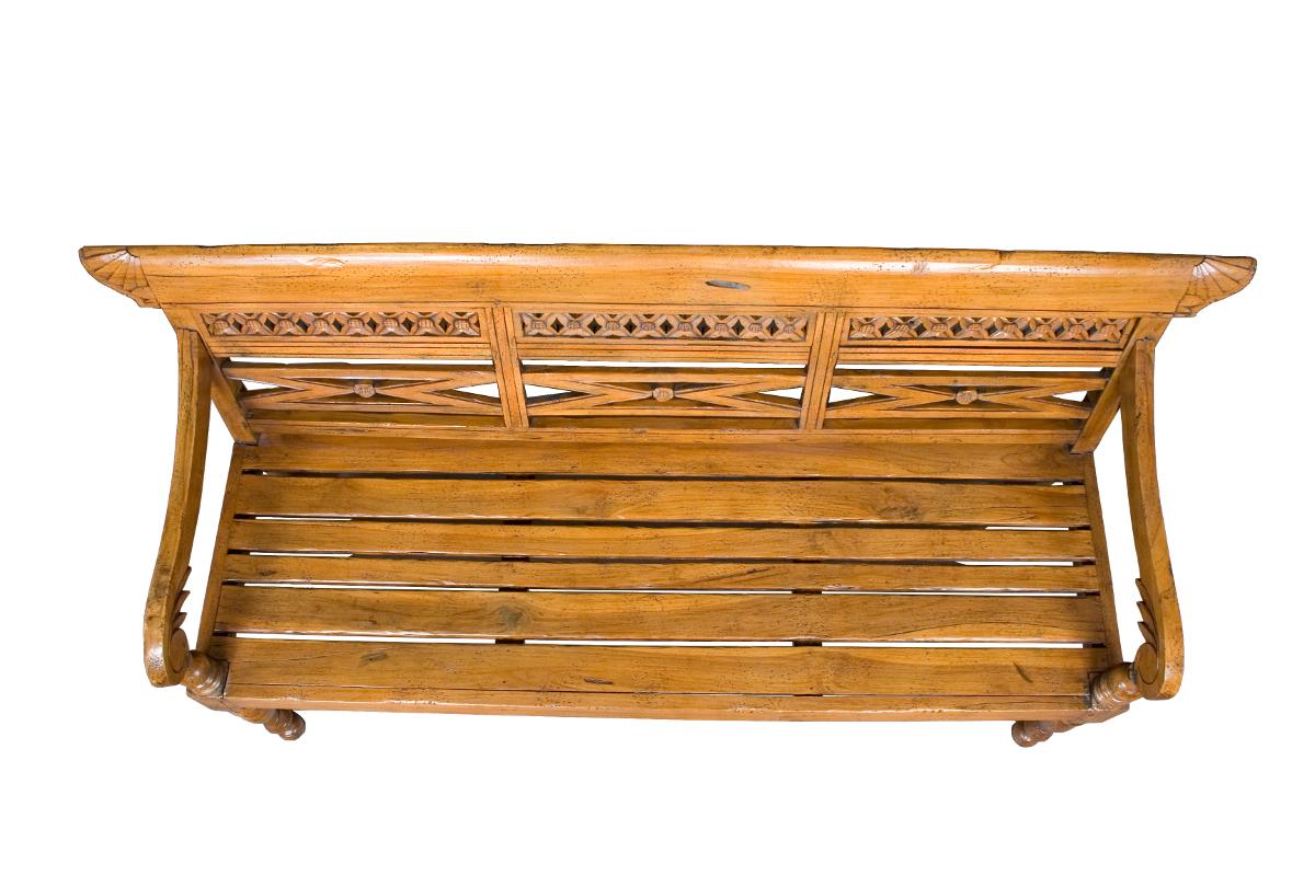This charming carved wood bench was made in England sometime around the year 1980 out of reclaimed pine wood. The result is a rustic and distressed looking bench that is very sturdy and well made. Turned front legs rise into flowing arm rests that