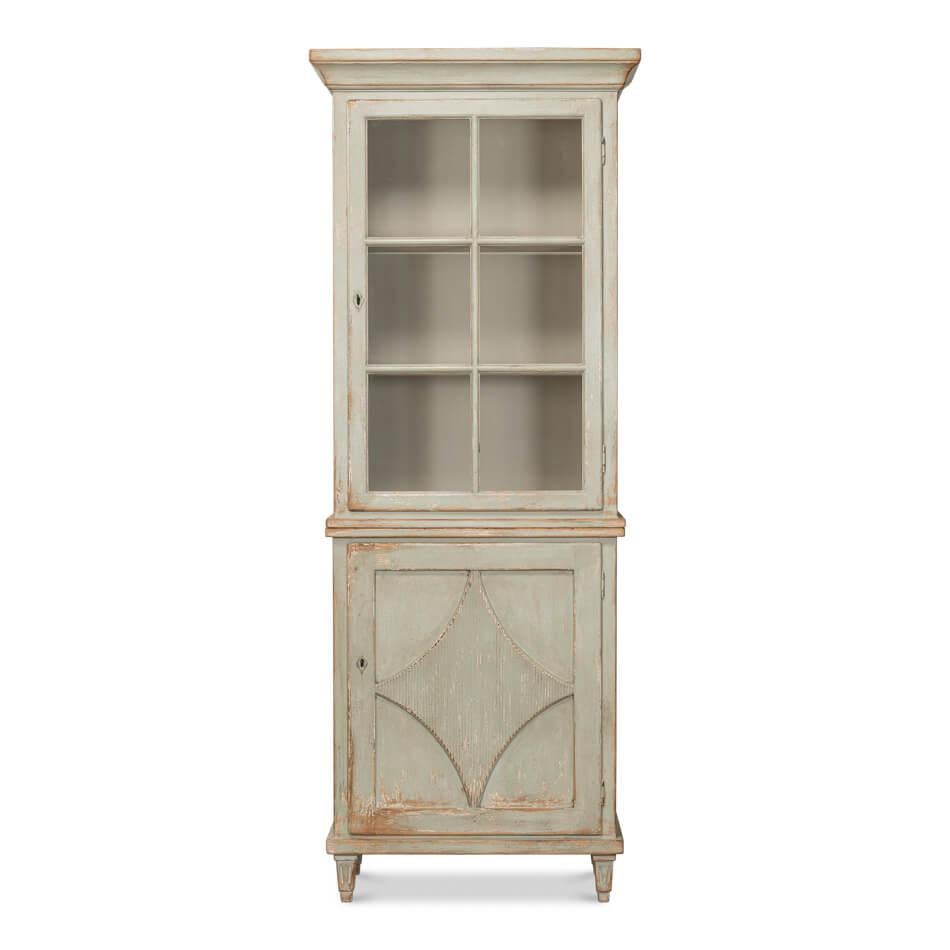 Made of pine with a distressed and antiqued sage painted finish, this cabinet exudes rustic charm.

The upper section, featuring glass-paneled doors, is perfect for showcasing cherished collectibles or books. Below, a solid door adorned with a