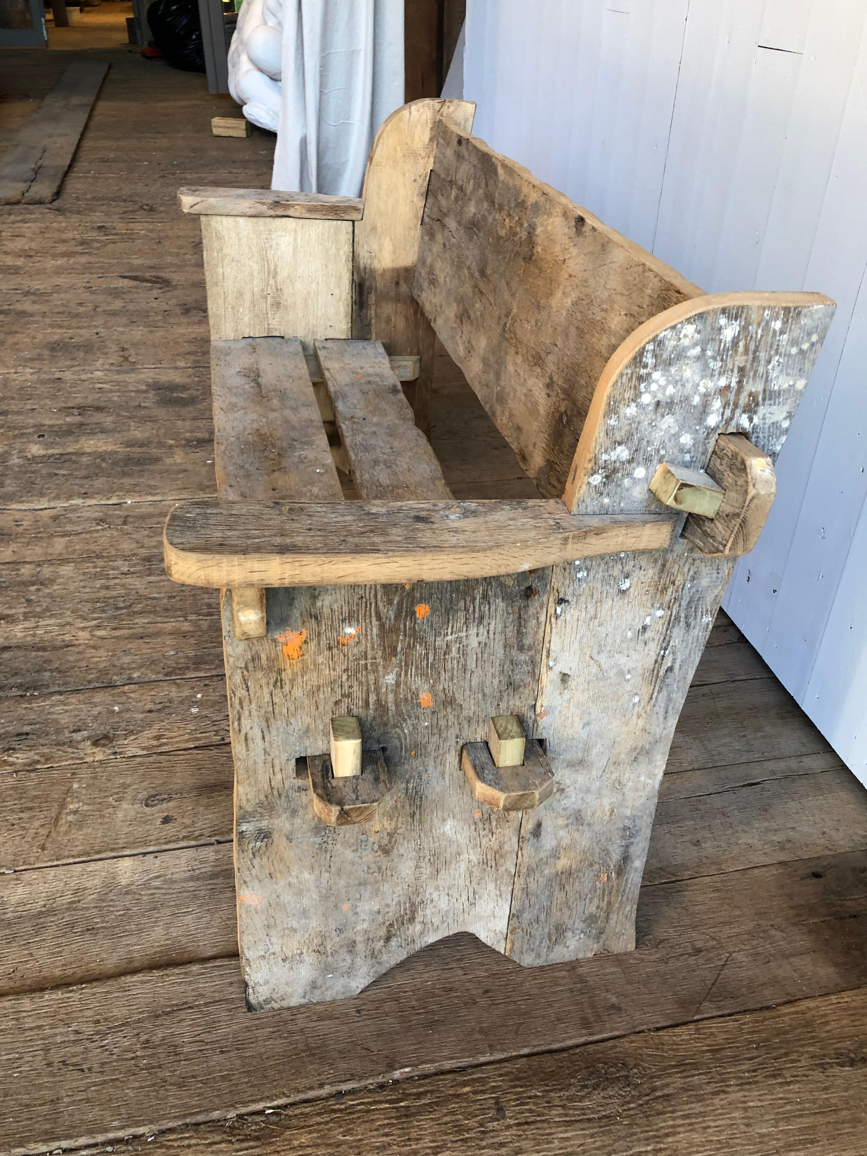 A rustic 2-seat bench in antique barnwood with traces of old grey painted finish with other colors, based on a traditional “knock-down” Scottish design, the bench is handcrafted and is easily disassembled by removing 6 tapered wedges on the sides.