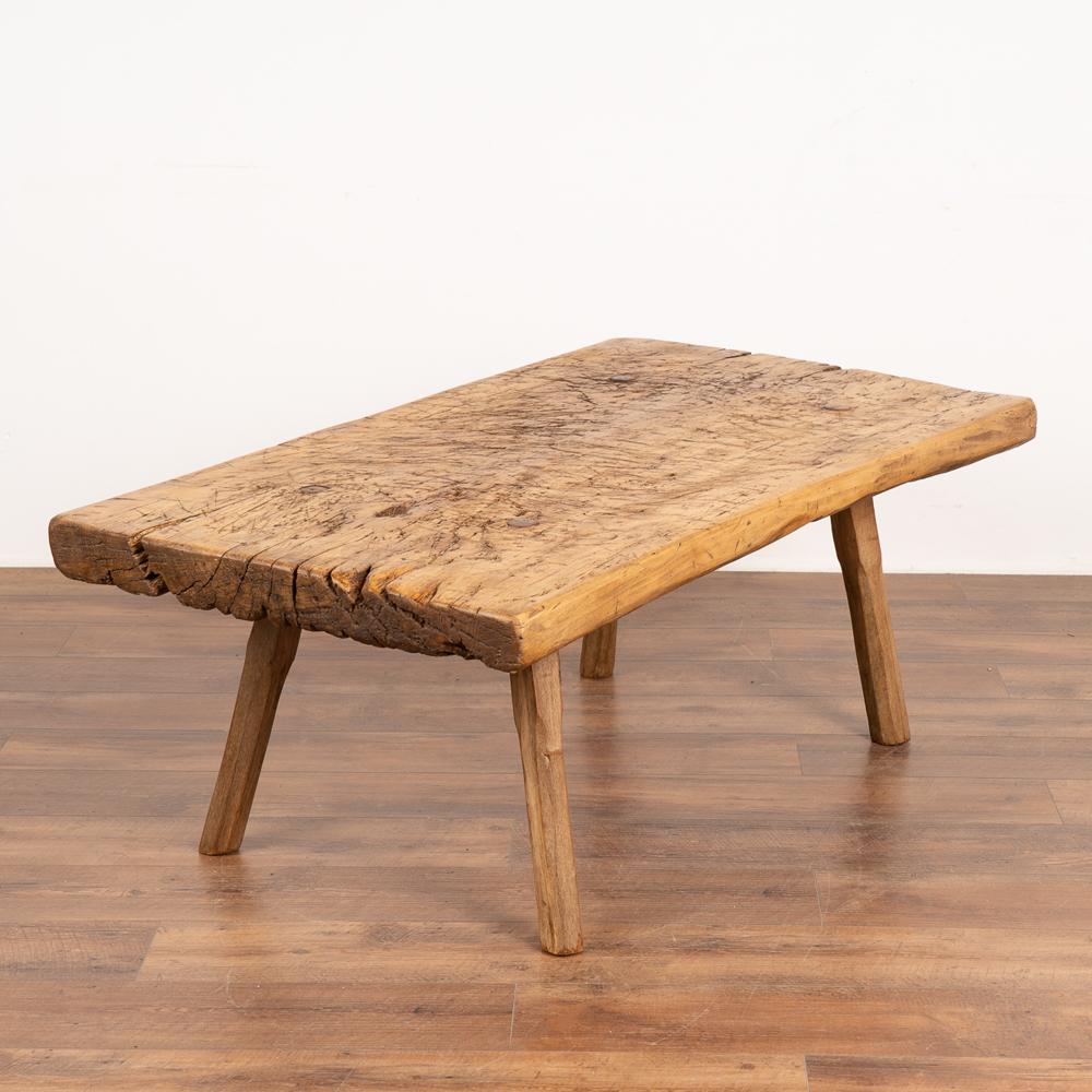This rustic slab wood coffee table with peg legs is loaded with vintage character due to the heavily distressed wood of the top.
The thick top is covered in scrapes, deep gouges, cracks, stains and markings acquired with over 100 years of use as a