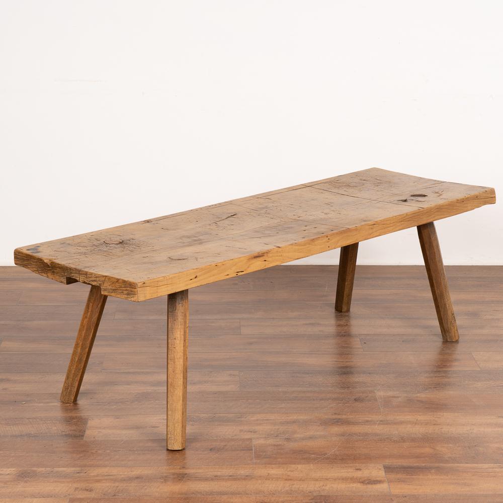 This rustic slab wood coffee table with peg legs is loaded with vintage character due to the heavily distressed wood.
The thick top is covered in scrapes, gouges, cracks, stains and markings acquired with over 100 years of use as a work